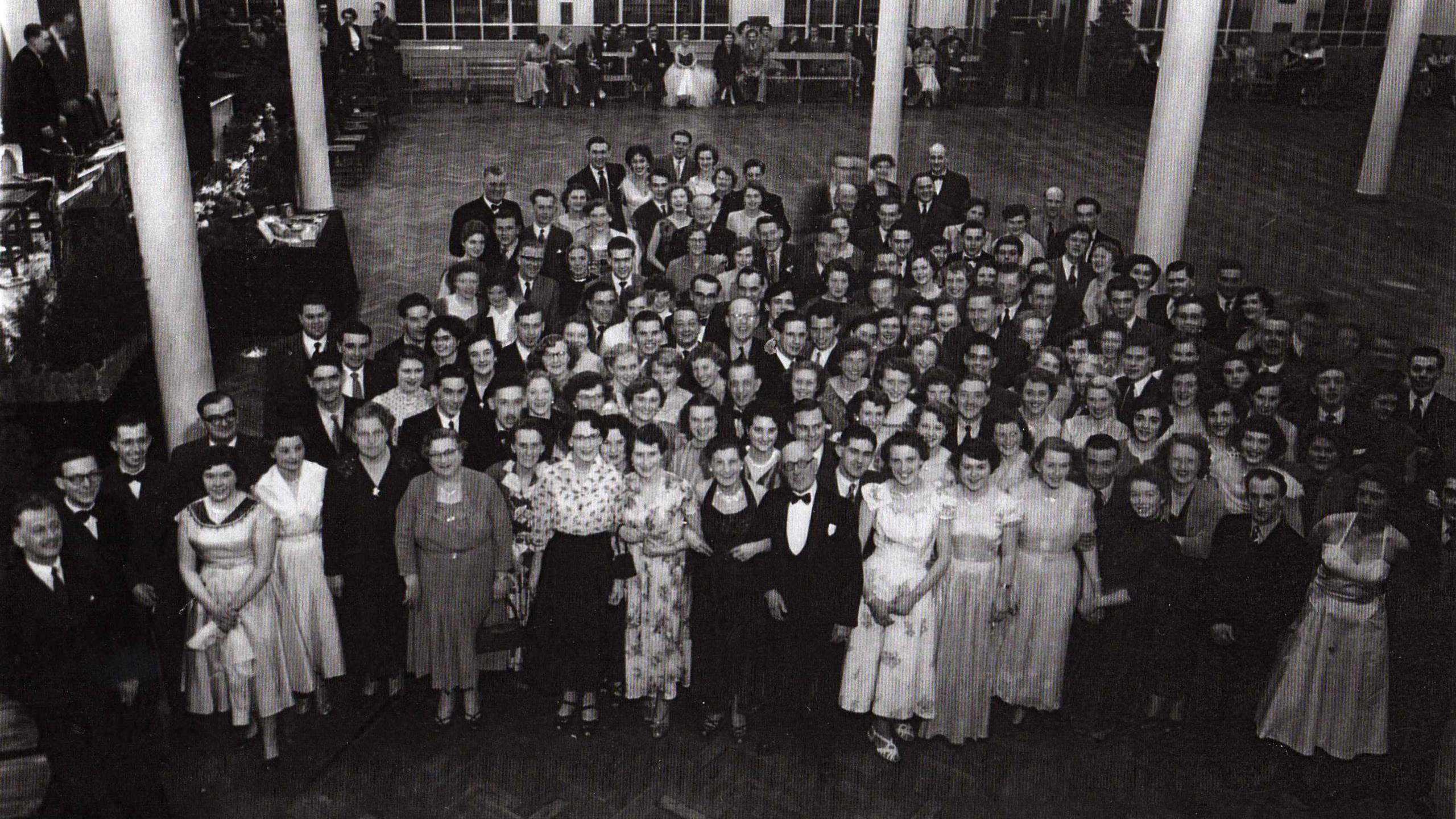 A large group of people dressed in suits and dresses looking up at the camera while at an event.