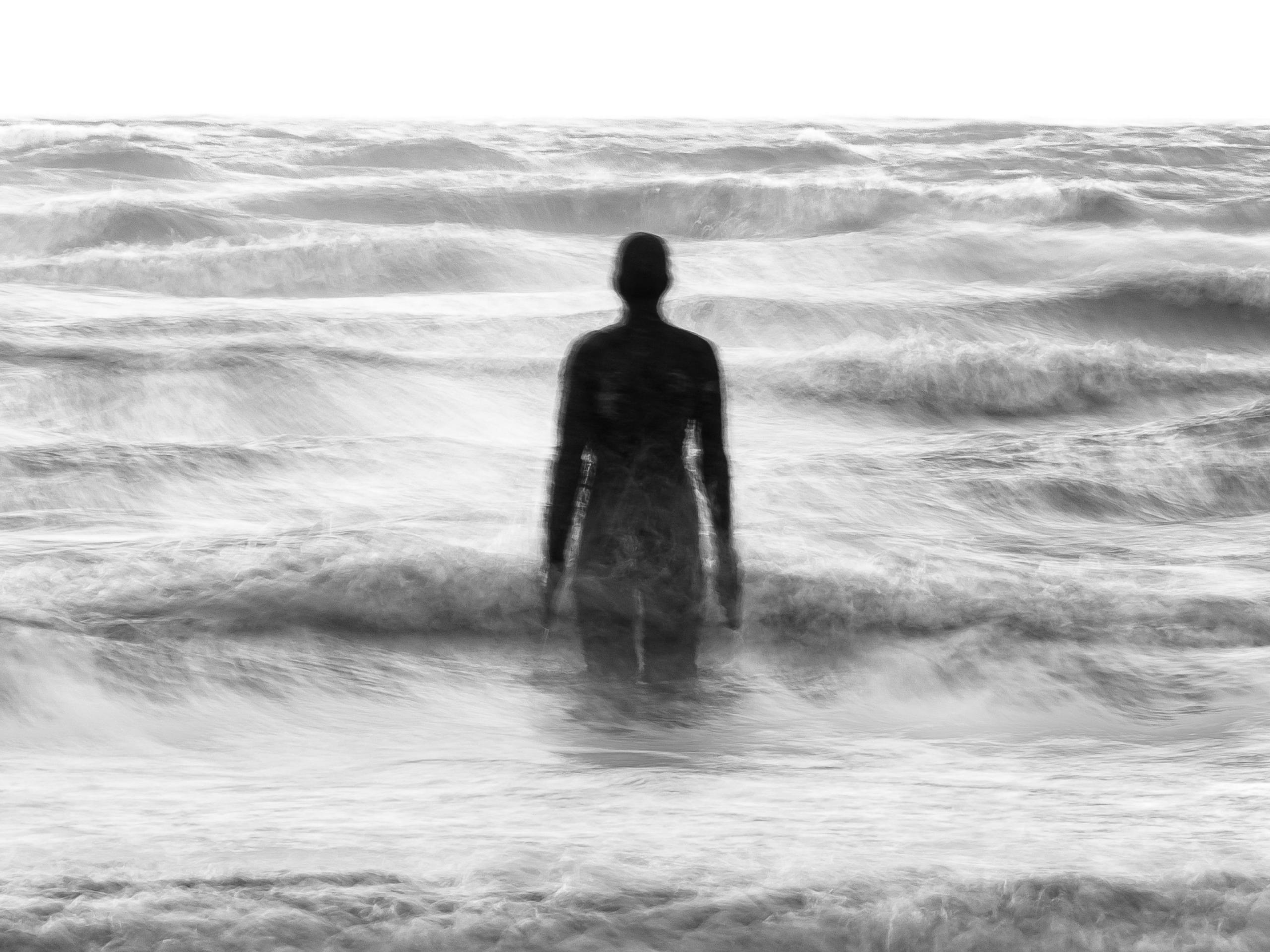 A statue stands in the sea as waves crash on the shore