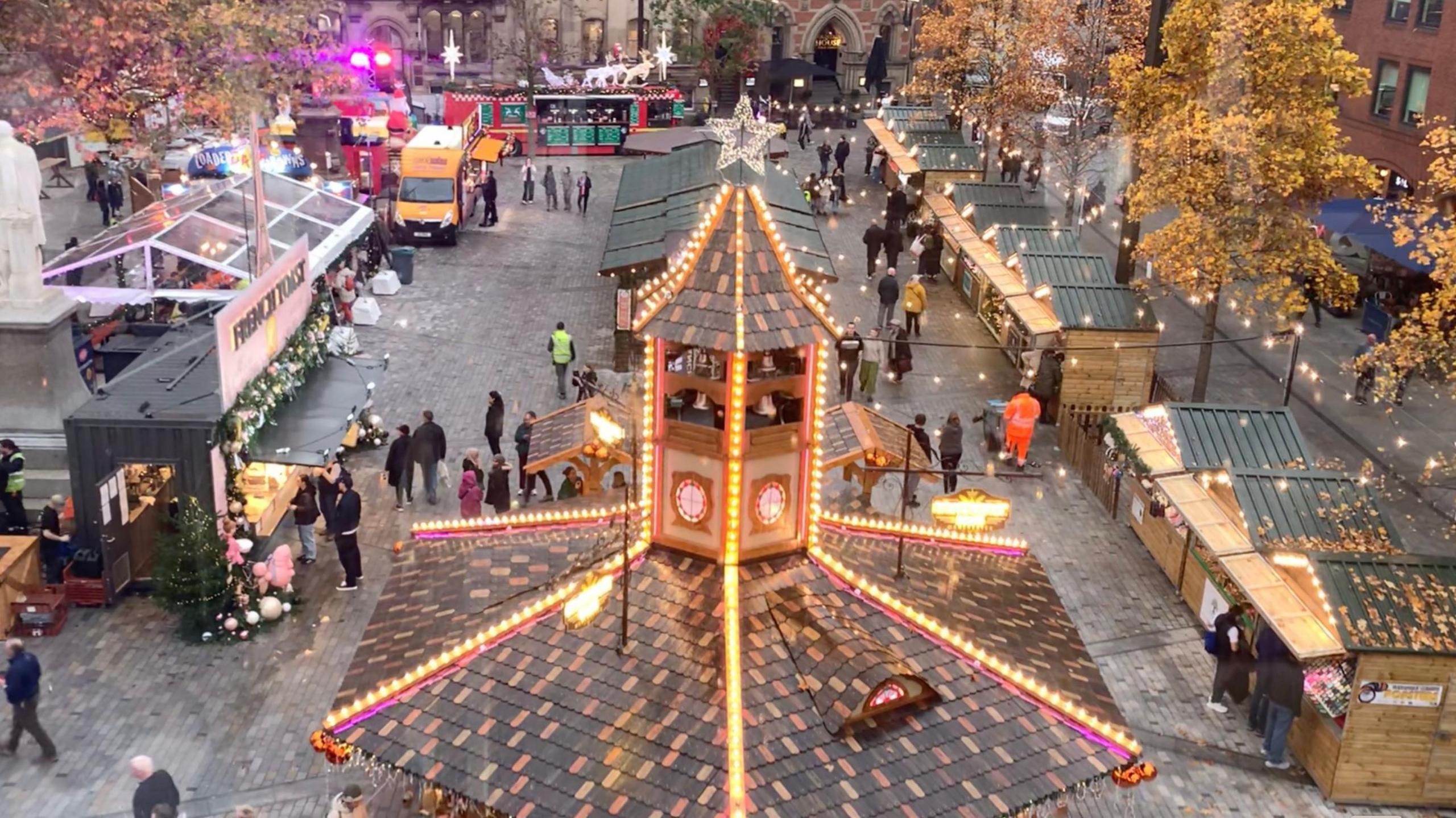 Picture taken out of the window of a ferris wheel, looking over a market with wooden huts and fairy lights below.