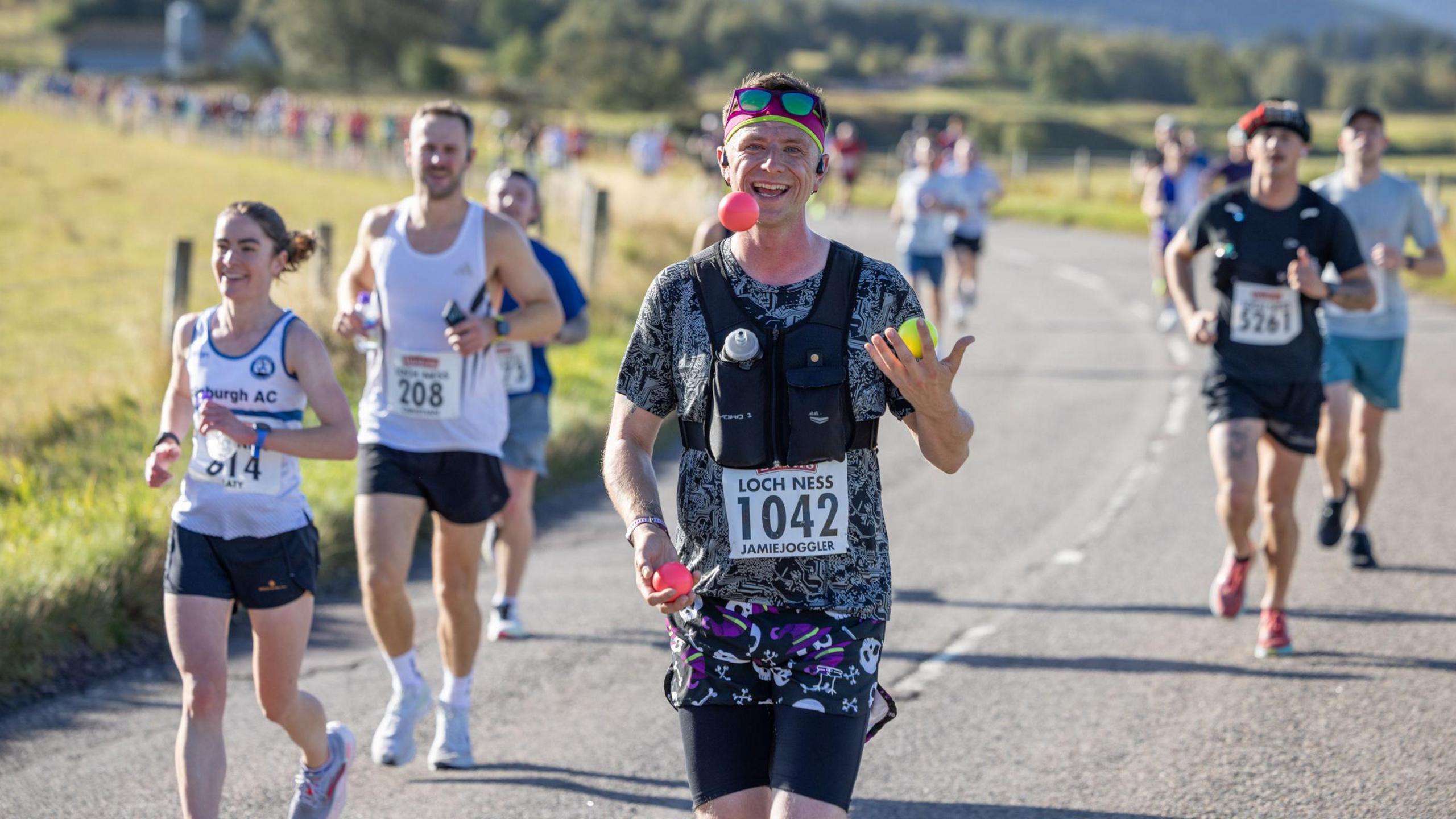 a man juggling balls as he runs with others along a road