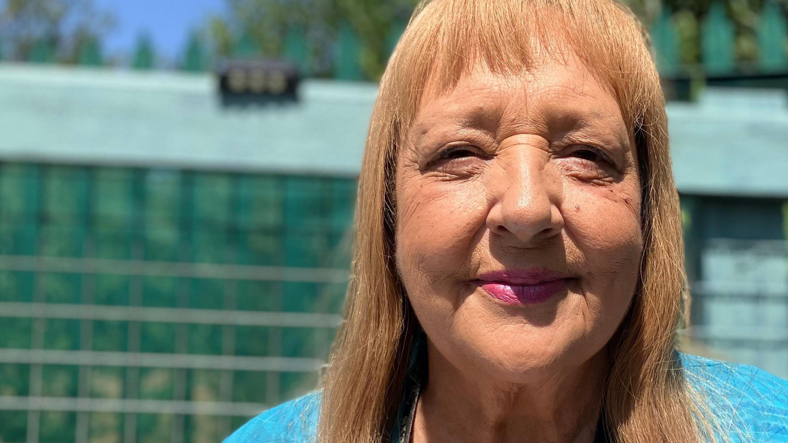Linda, a woman with shoulder-length golden hair, wearing a blue top, smiling for the camera.