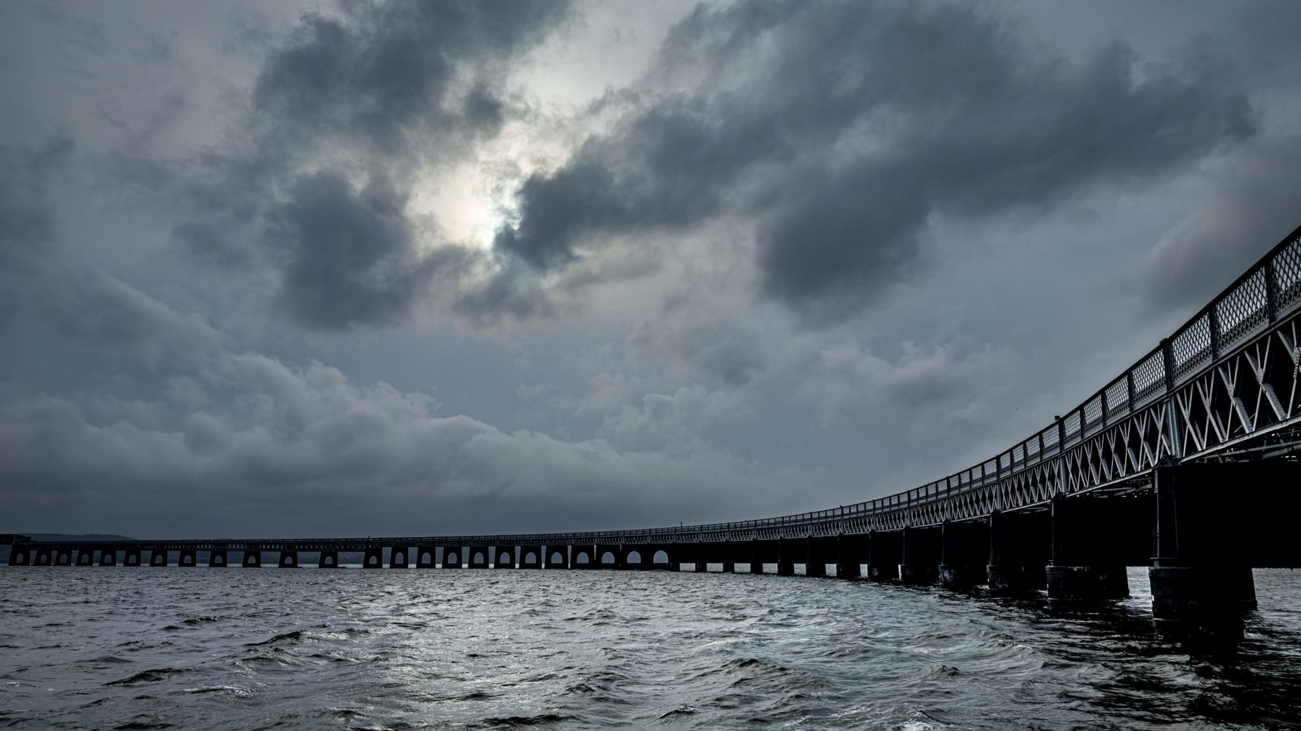Dark clouds gathered over a bridge with the sea underneath it