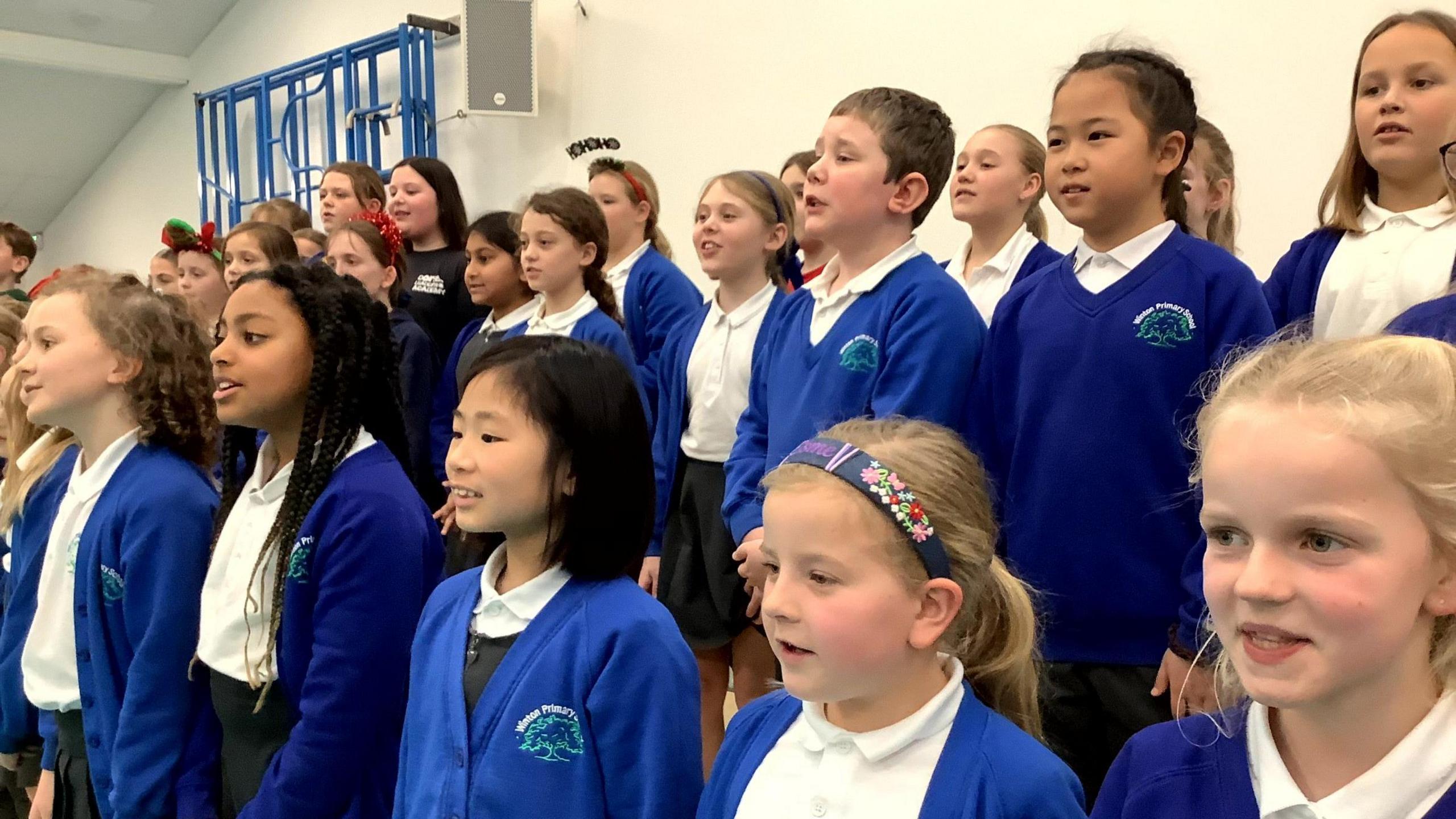 A group of children singing in blue and white school uniform.