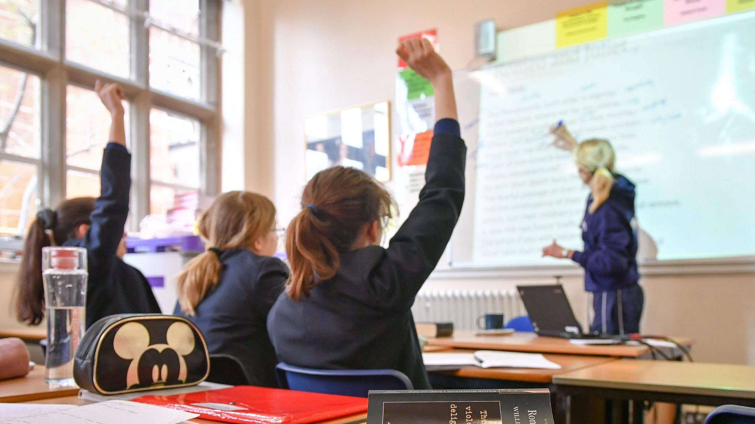 Female schoolchildren sat in a classroom, with a female teacher writing on the board. 