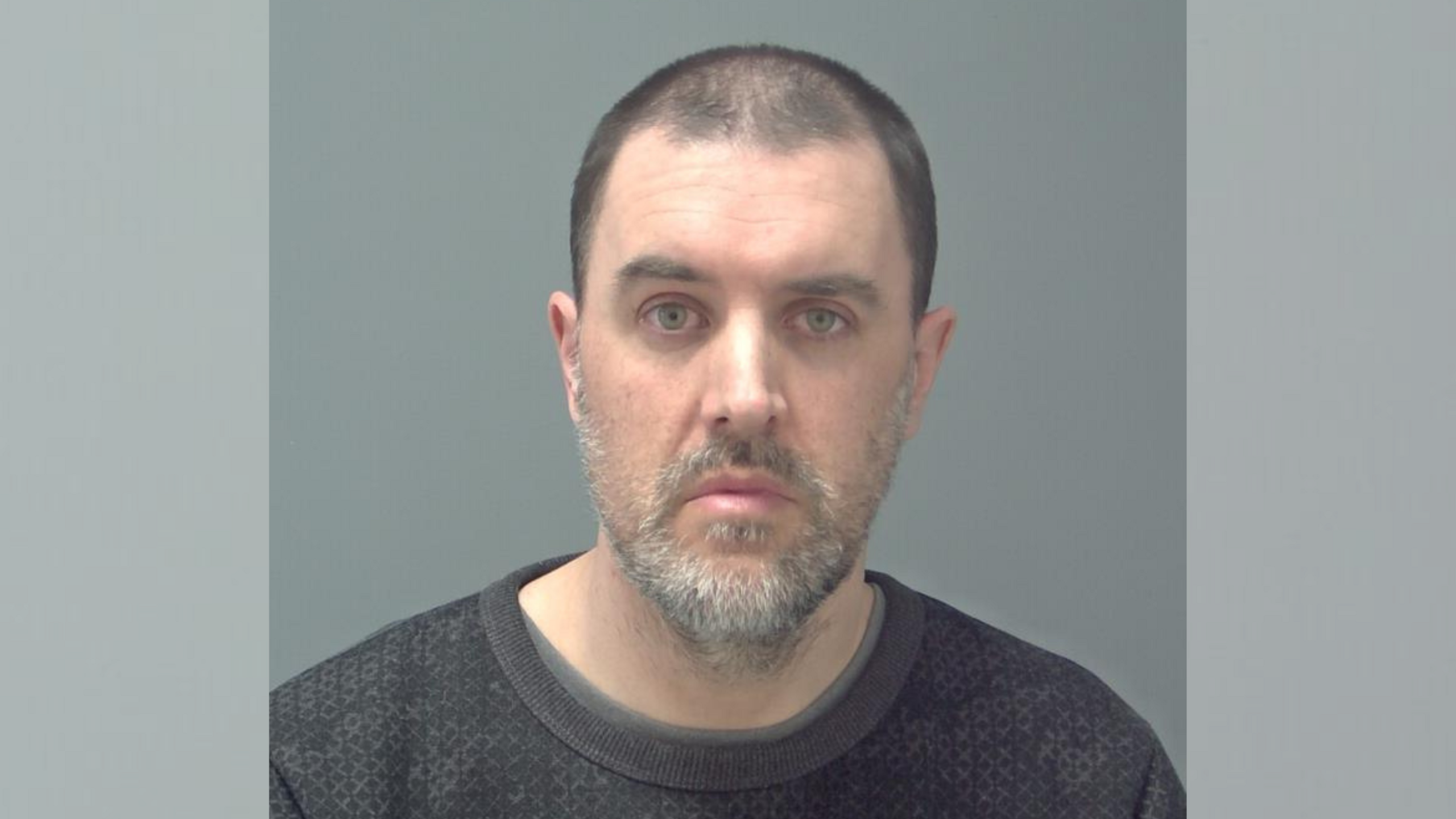 A police custody mugshot of Martin Woods - a man with shaven black hair and grey/white facial hair