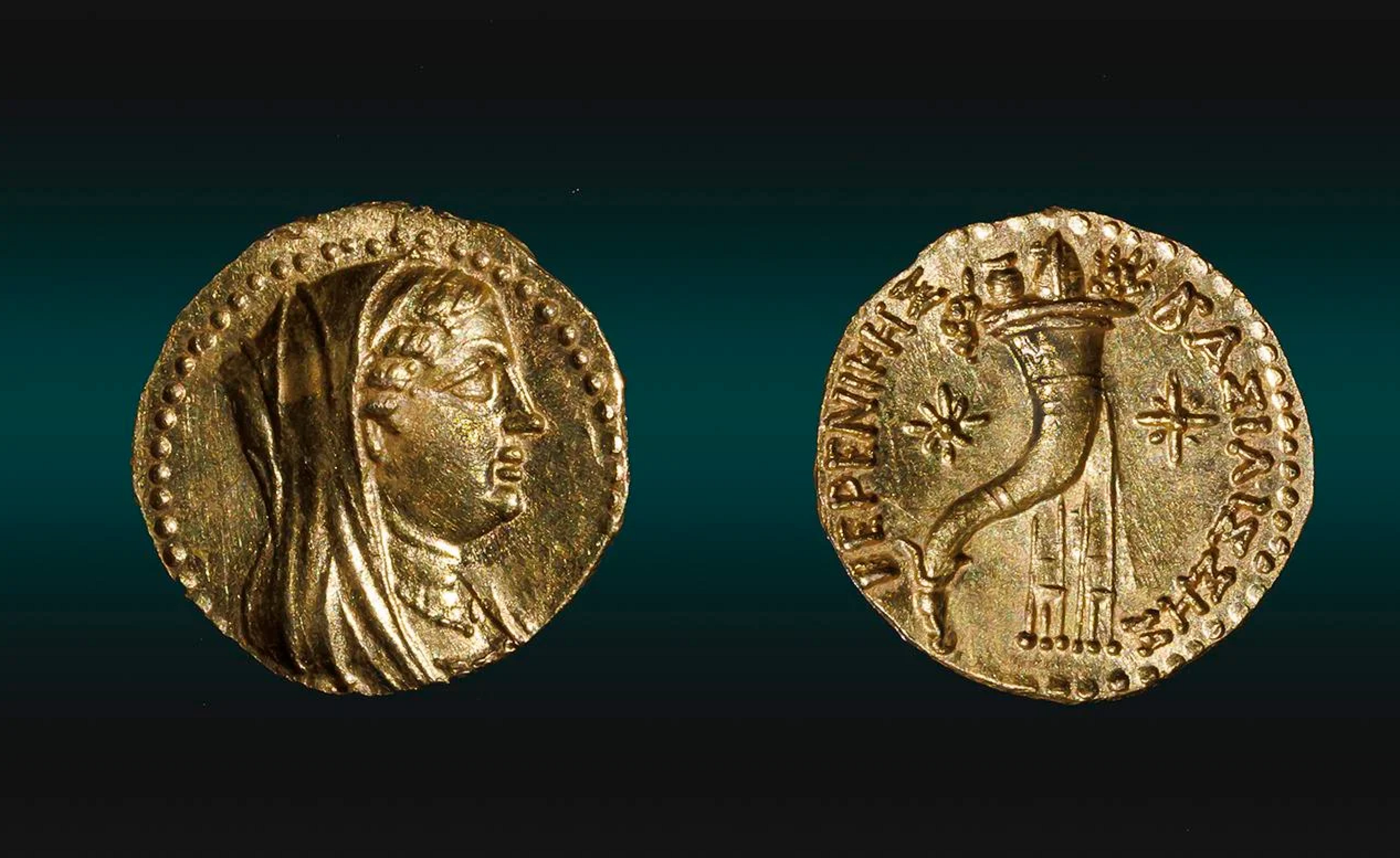 One side of the gold coin showing Queen Berenice wearing a tiara, a veil, and a necklace. The other side shows two stars and a cornucopia, also known as the "horn of plenty' - typically shown as a curved, horn-shaped basket overflowing with fruits, vegetables, and flowers.
