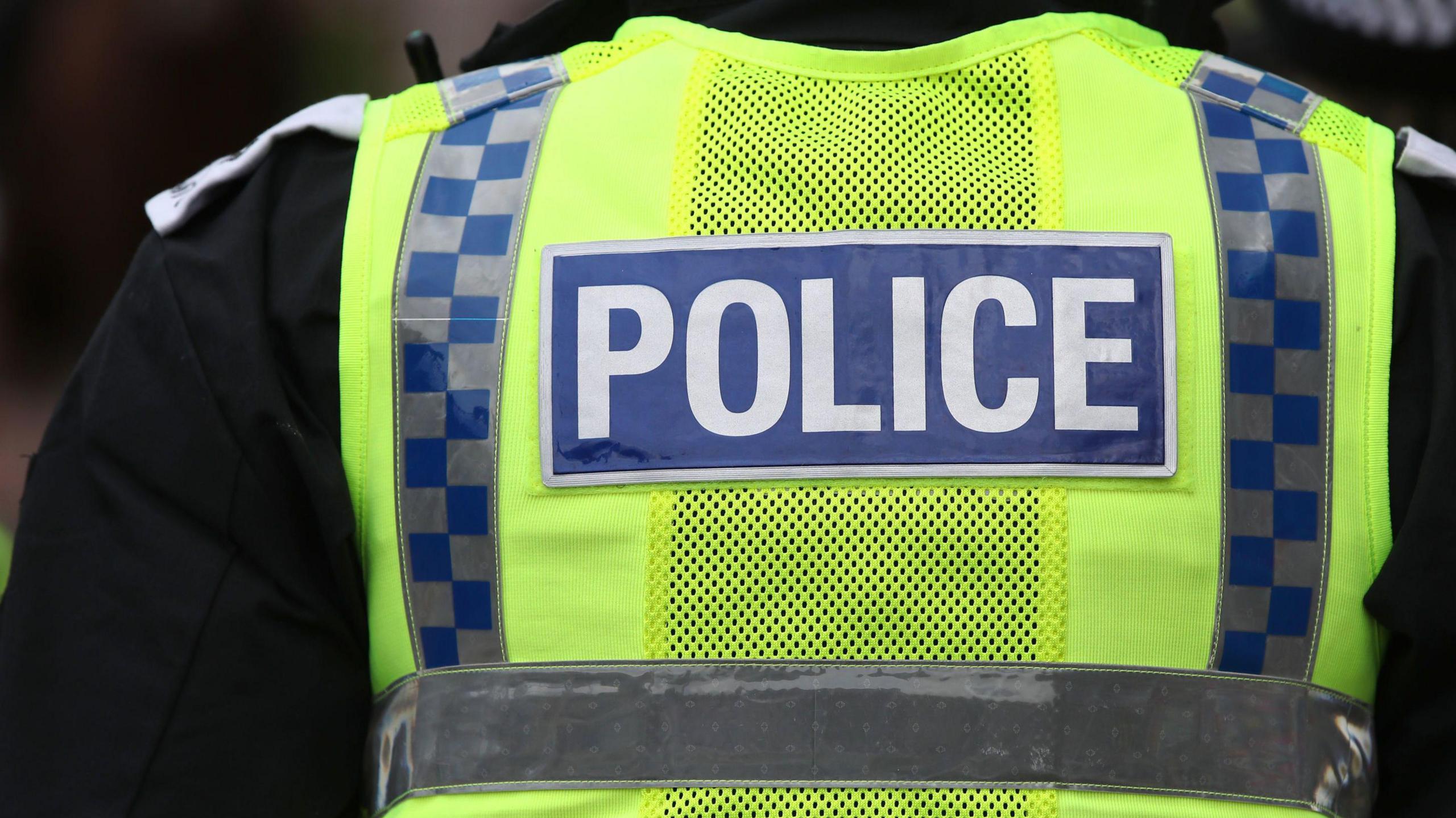 The back of a high visability green police vest with the word 'Police' written across the middle. 