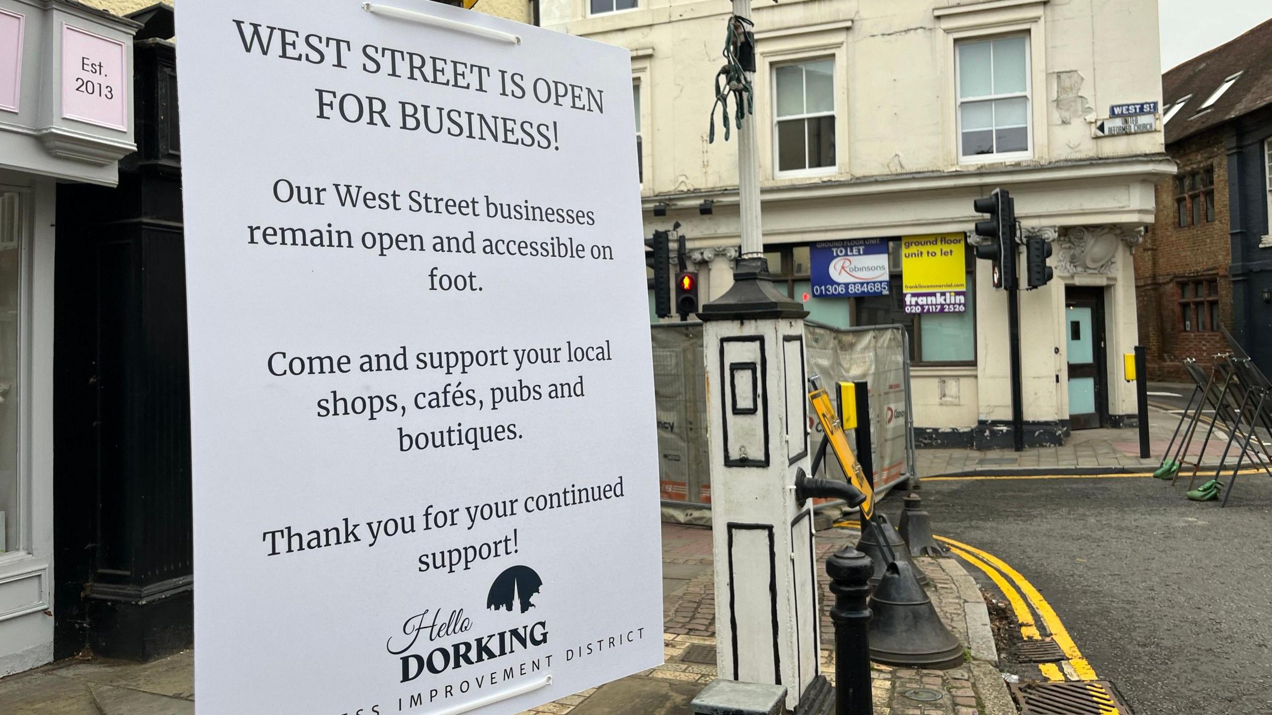 A sign which reads West Street is open for business and encourages people to continue visiting shops cafes and pubs on foot while the road is closed to cars