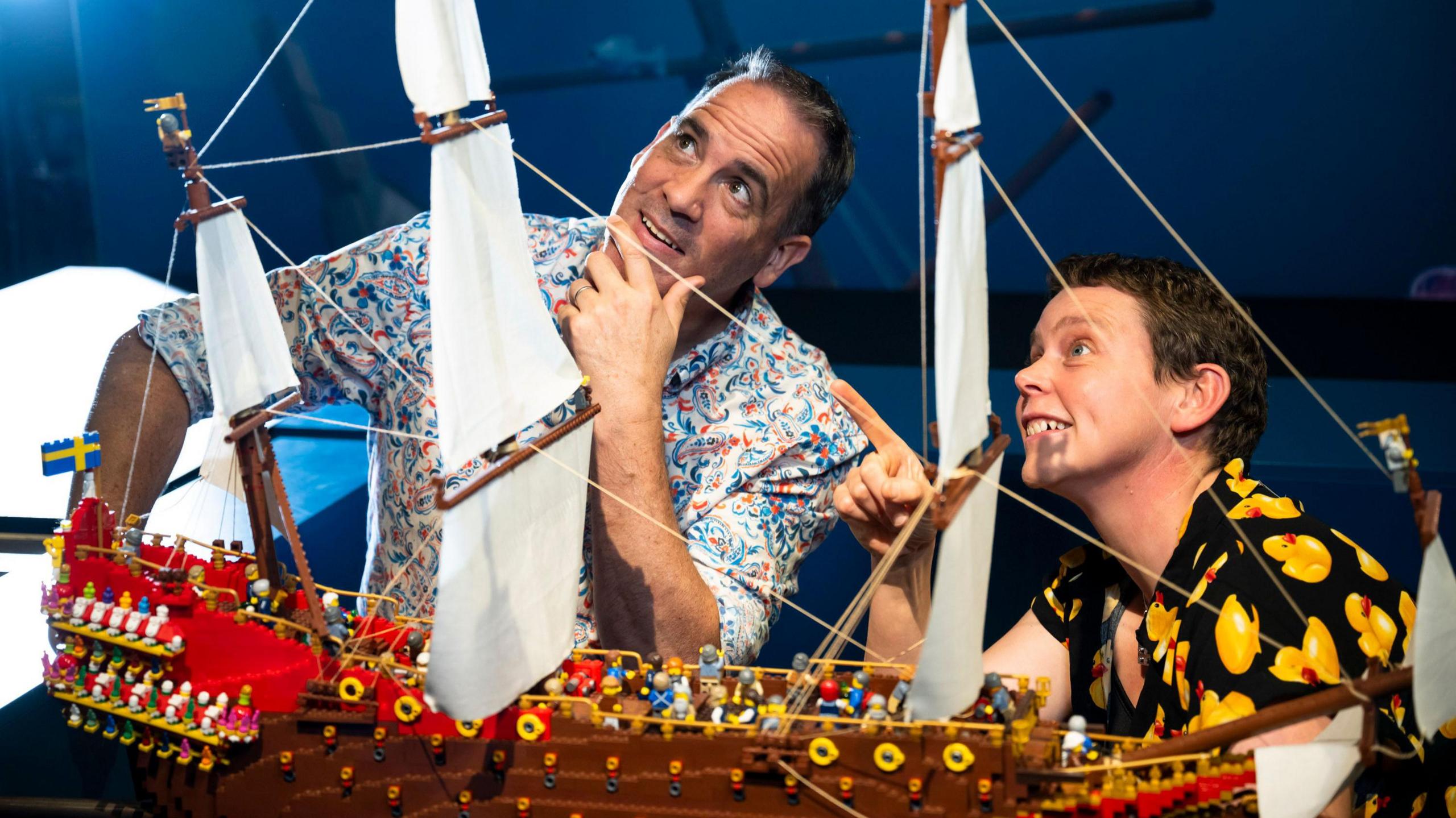 A lego model of the shipwrecked ship Vasa with model builders Ryan McNaught and Em Blamey looking at it 