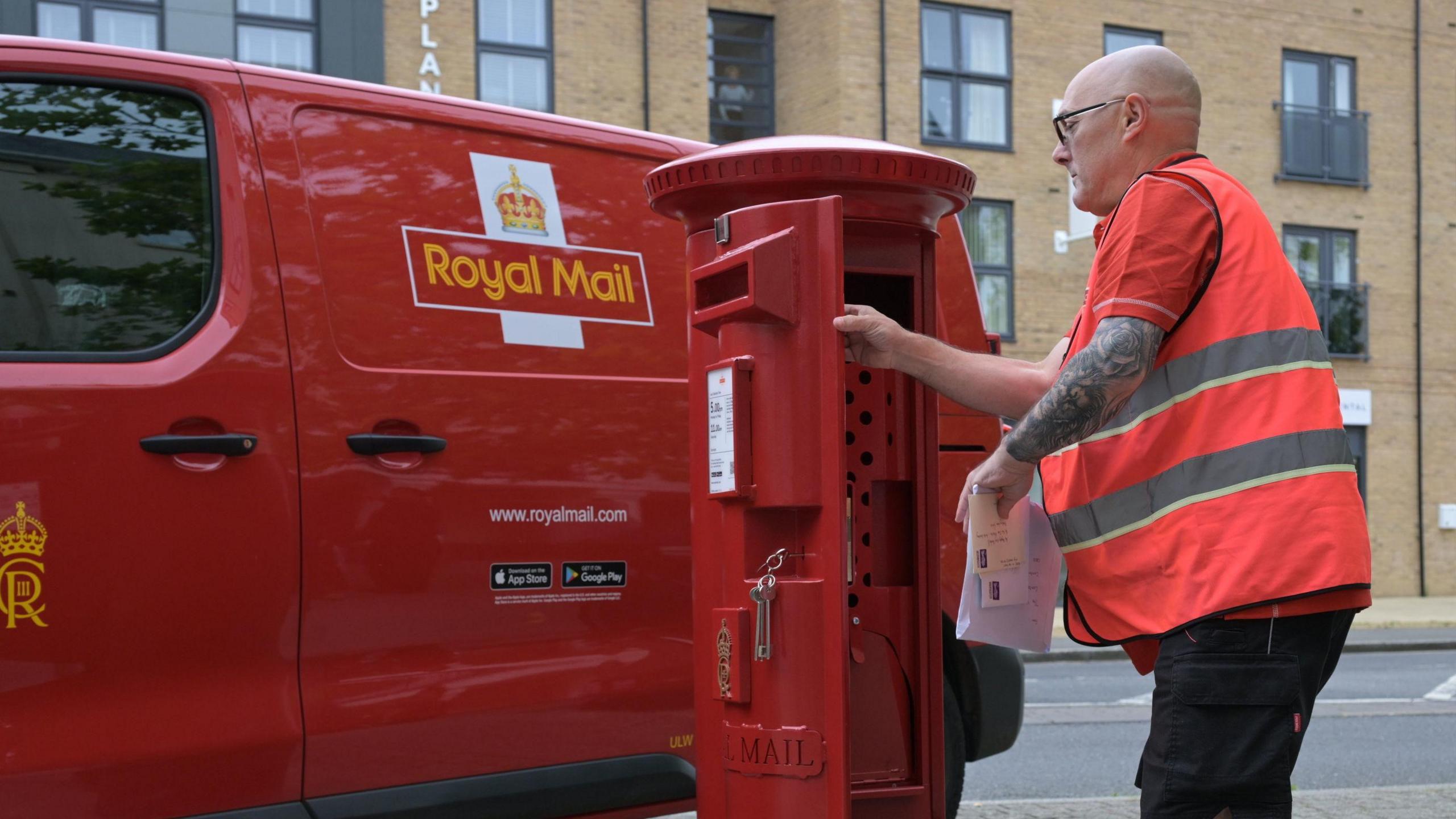 A postman is pictured opening a post box next to a parked Royal Mail van.