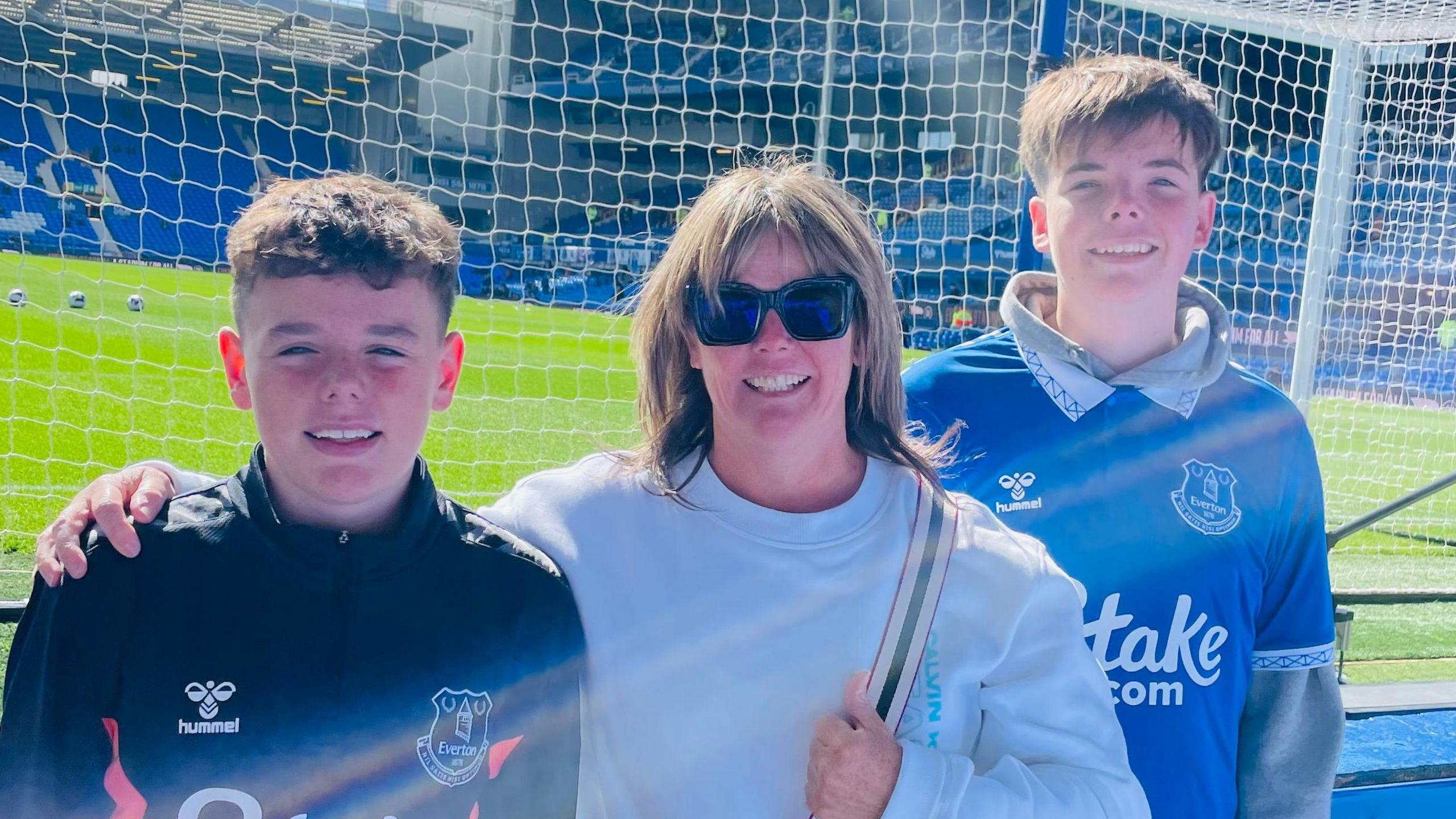 Group family picture of Rita, flanked by her two sons in Everton shirts, by the Goodison Park pitch.