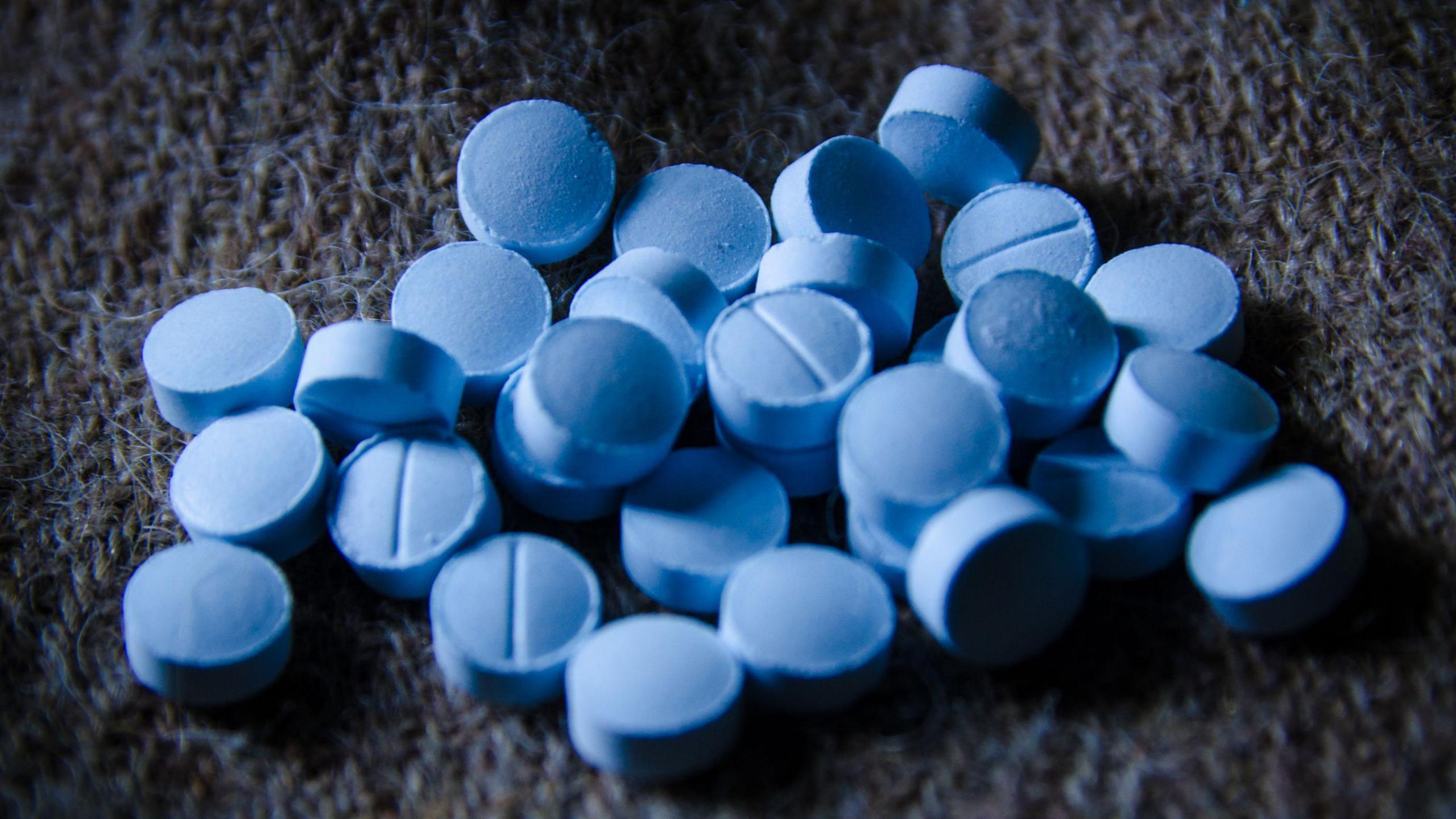 Several round bright blue pills scattered on a dark grey and blue fabric