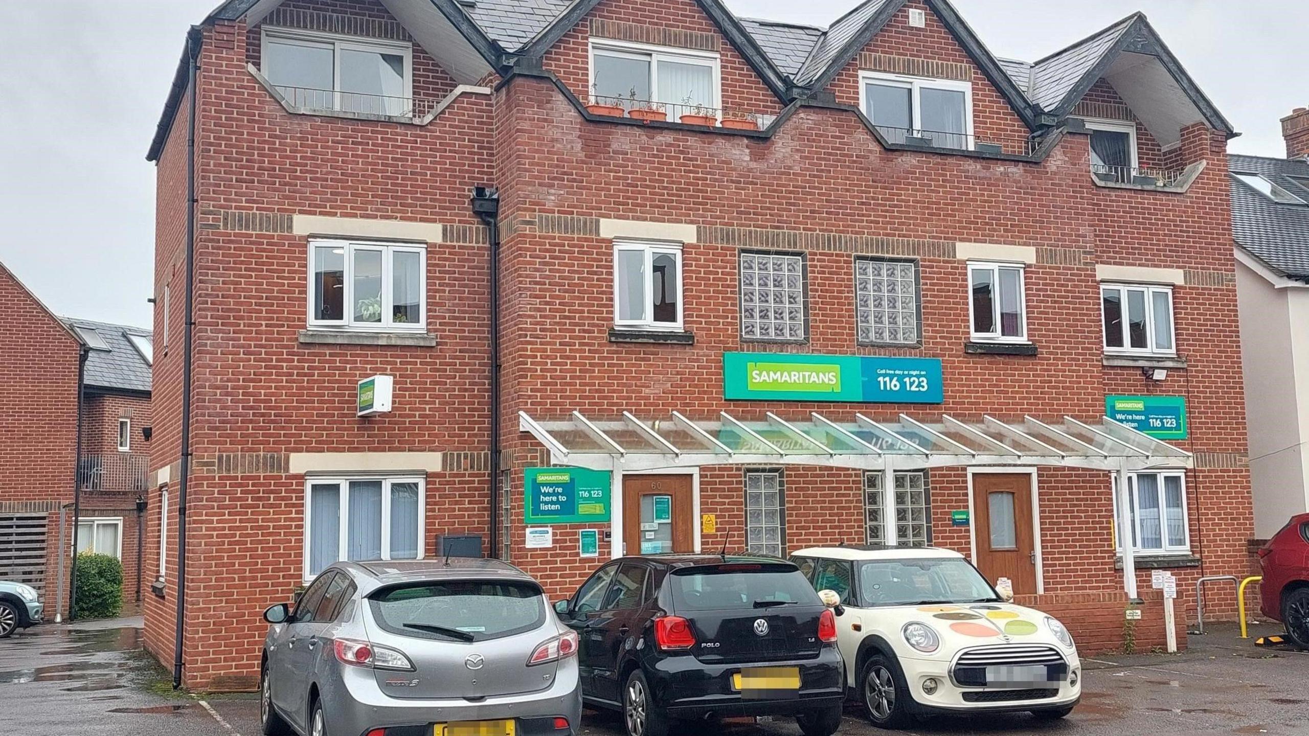 A three-storey brick building with a green Samaritans sign on the front