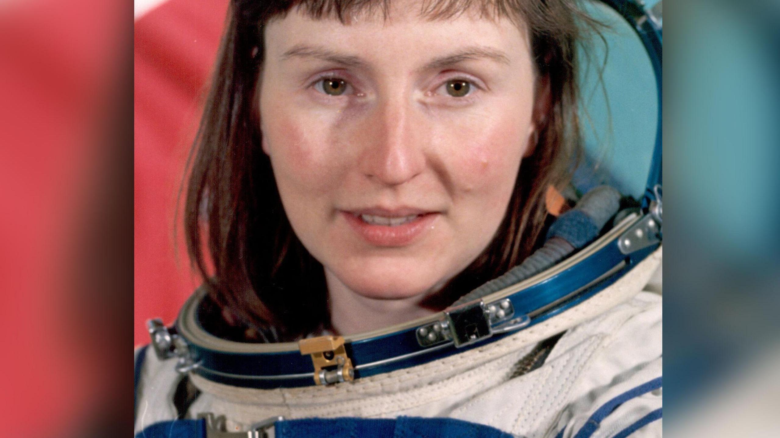 Helen Sharman seen in her official portrait for the Project Juno in 1991. She has long brown hair and is wearing a white space suit with an open domed visor.