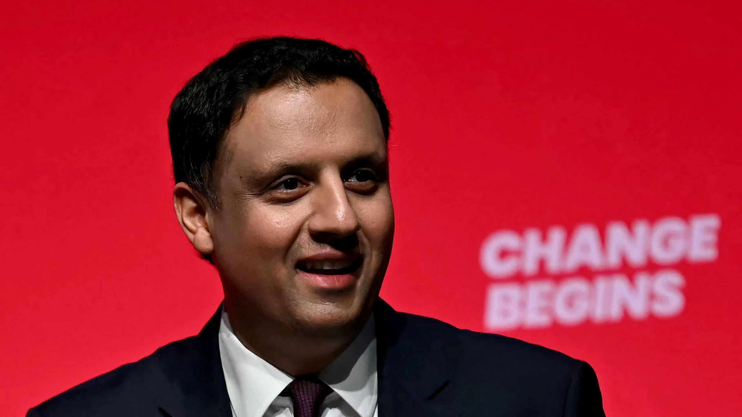 Anas Sarwar, dressed in a suit, speaking at the Labour party conference in Liverpool. A sign reading Change Begins in the background.