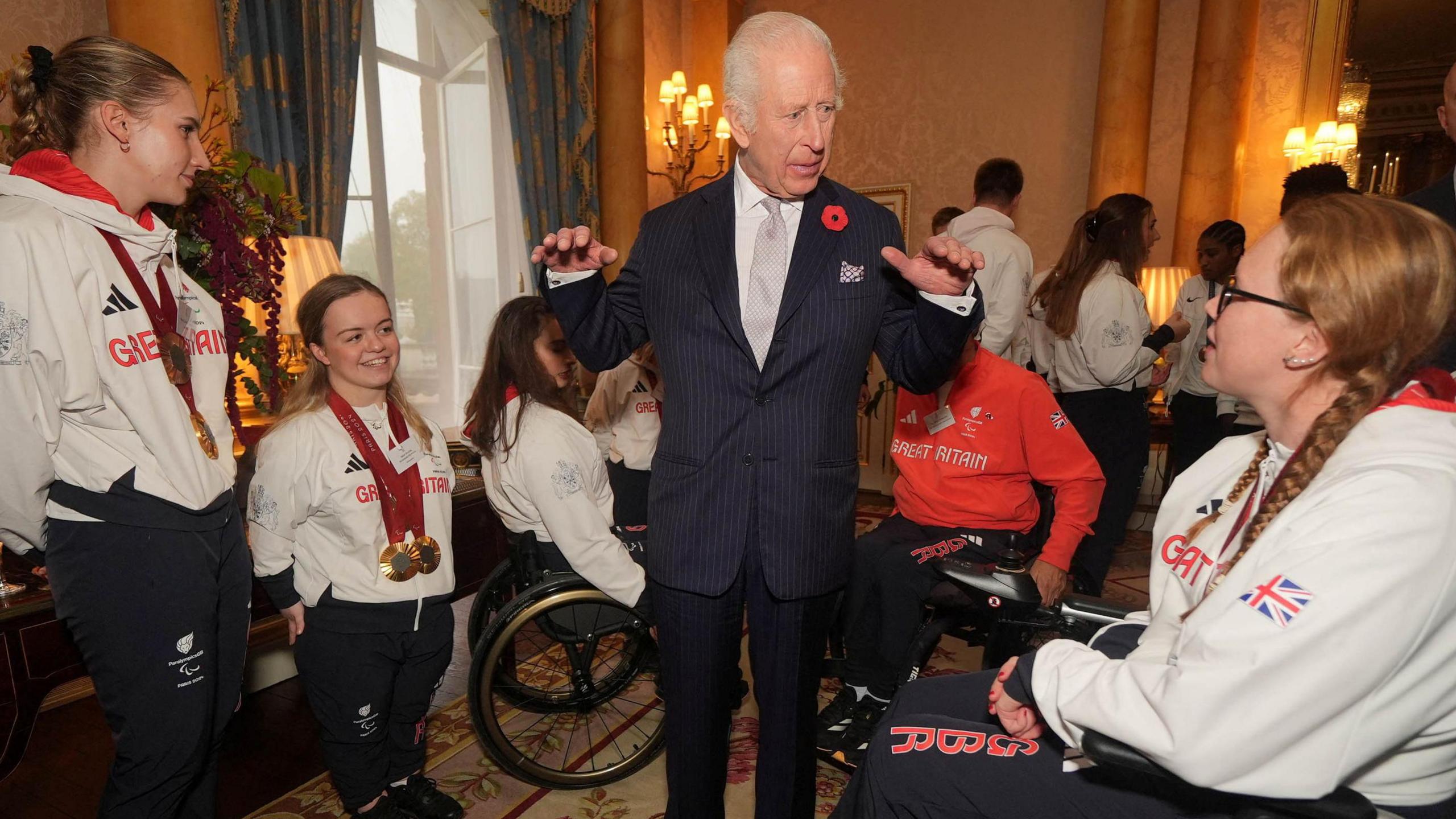 King Charles stands in the centre of a group of athletes wearing medals and GB tracksuits