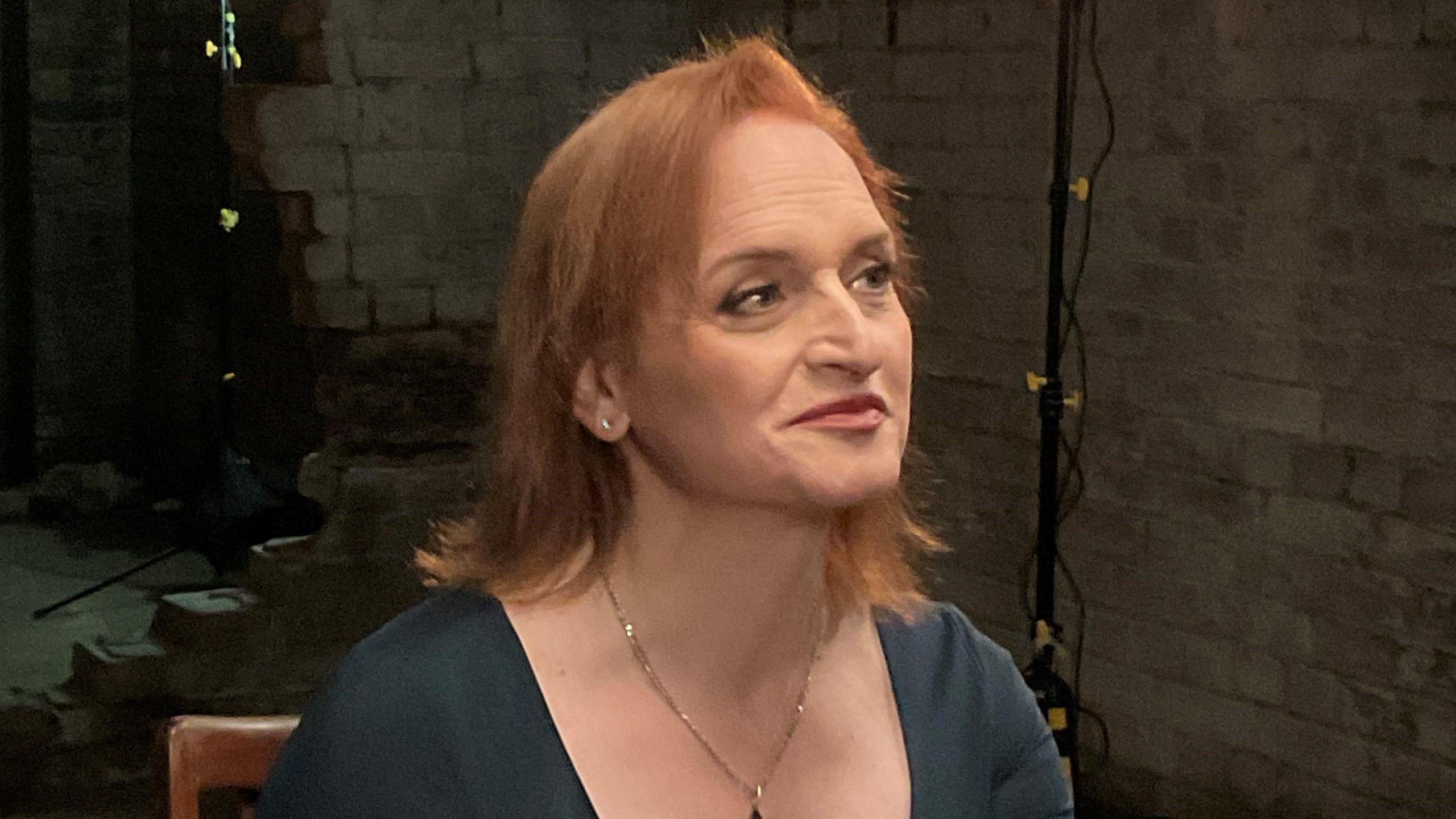 A woman with ginger hair looking to the right and smiling.