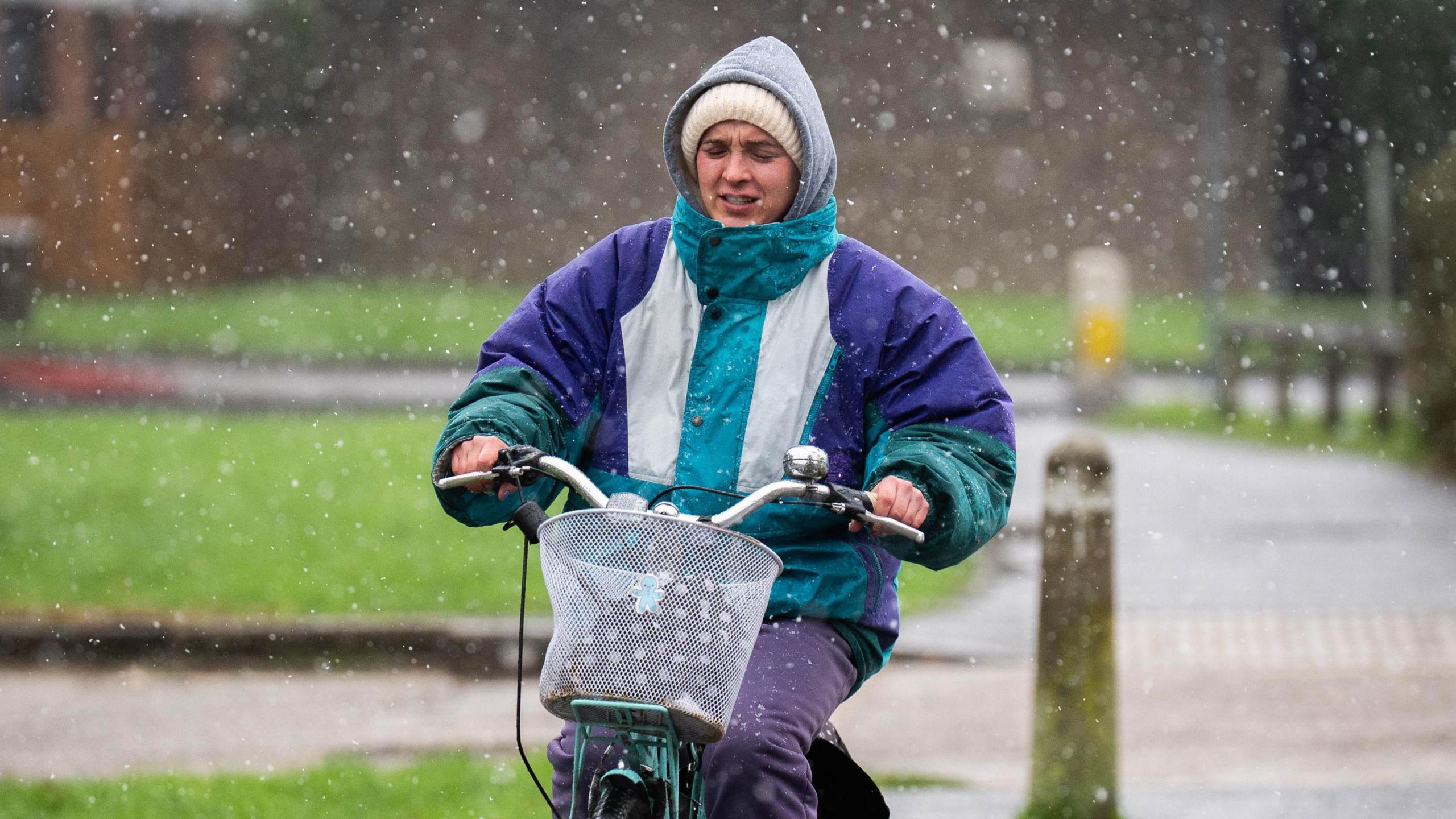 A woman wearing a rain jacket and a woolly hat riding a bicycle.