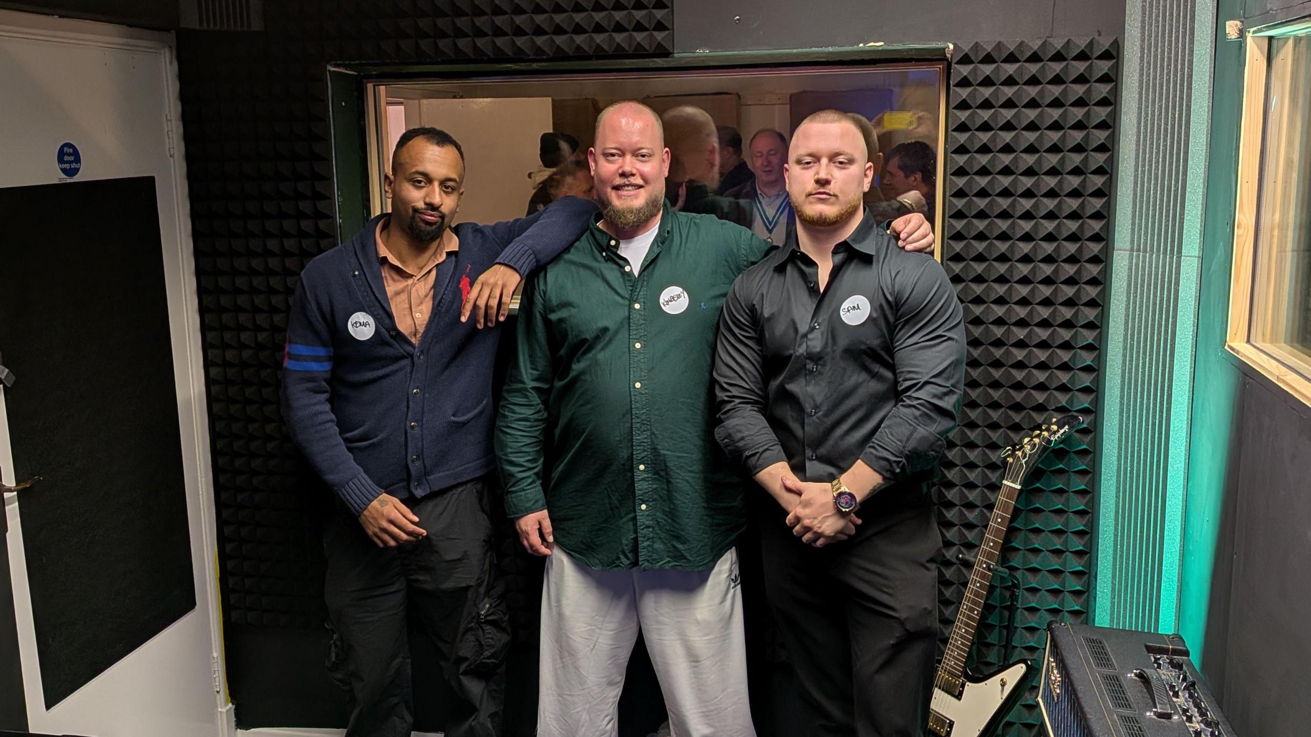 Three In-Spire workers stood arm in arm in a recording studio.