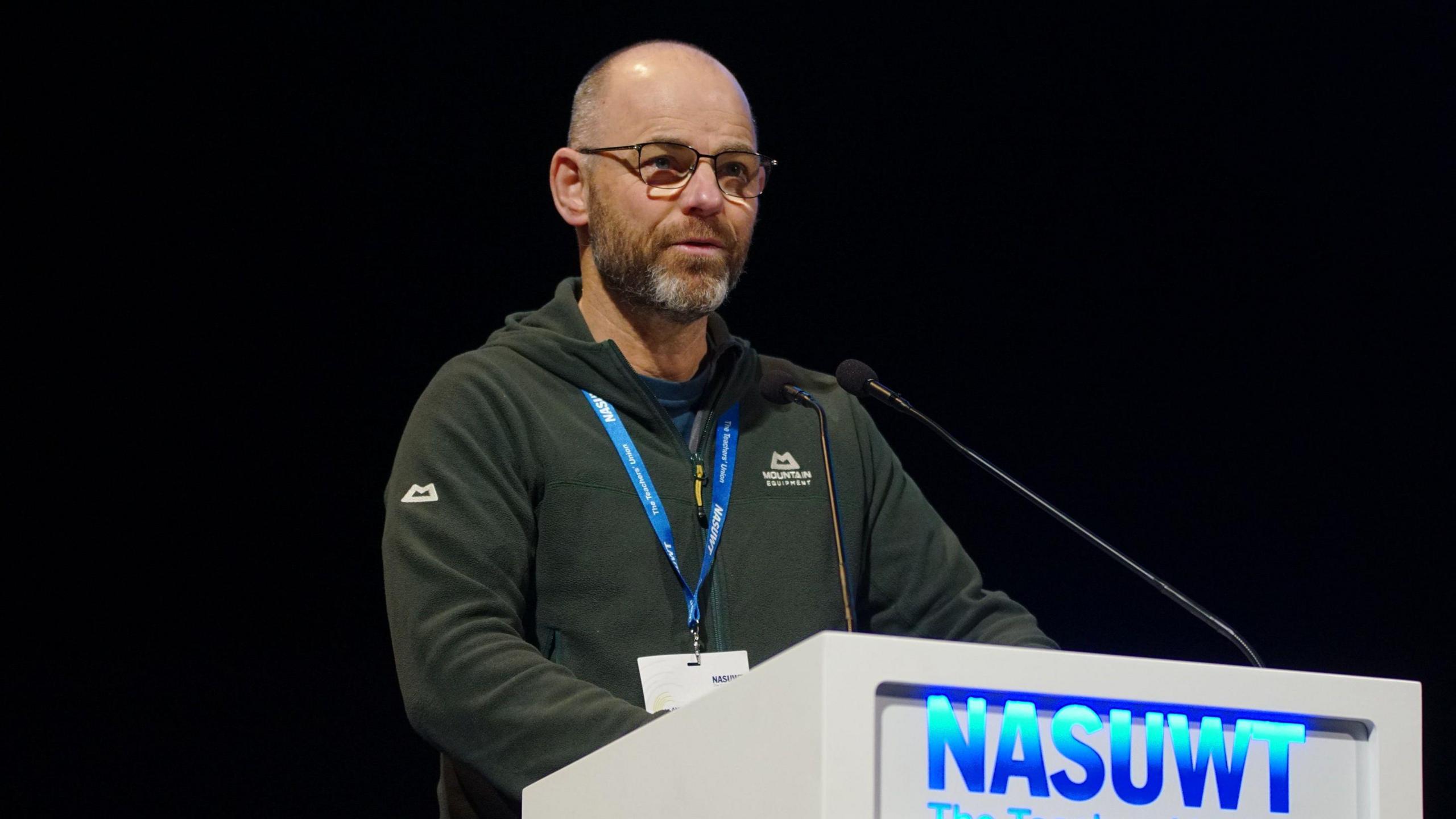 Richard Kempa with very short hair speaking from behind a NASUWT lectern