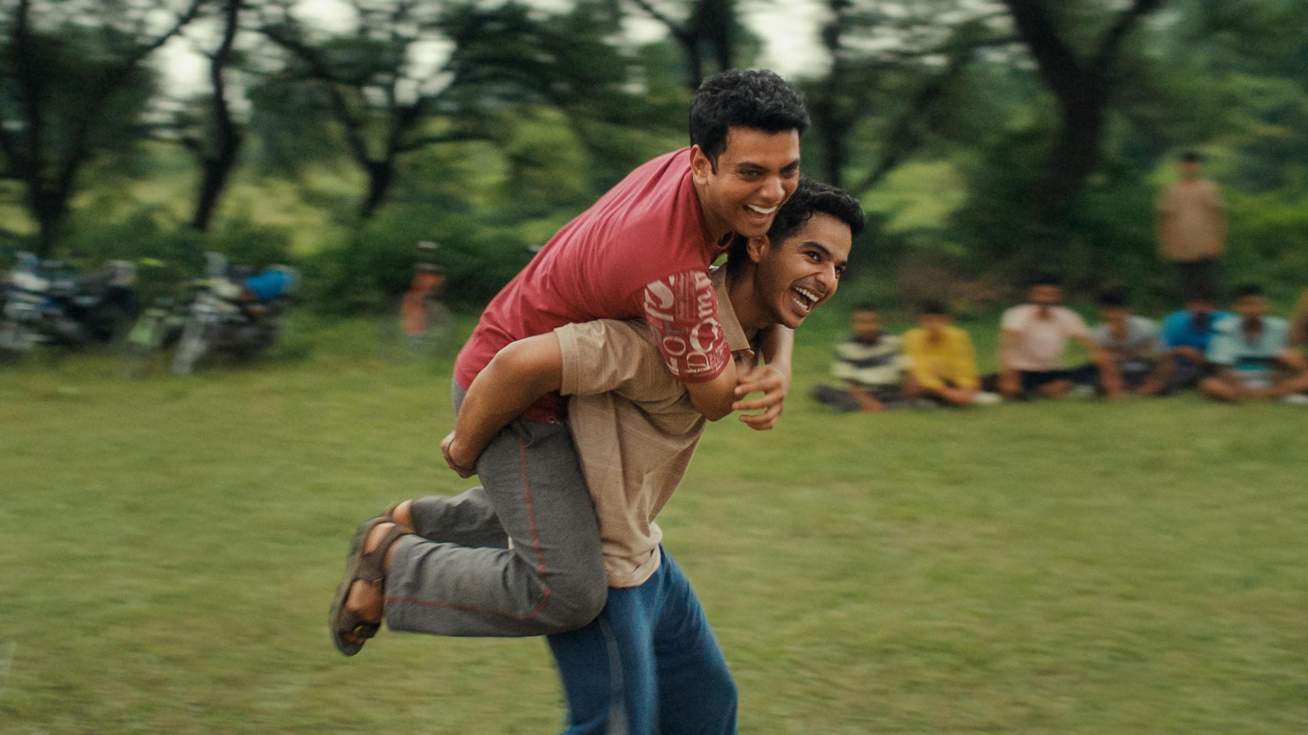 A still from the film Homebound which shows a man carrying another man on his shoulders on an open field