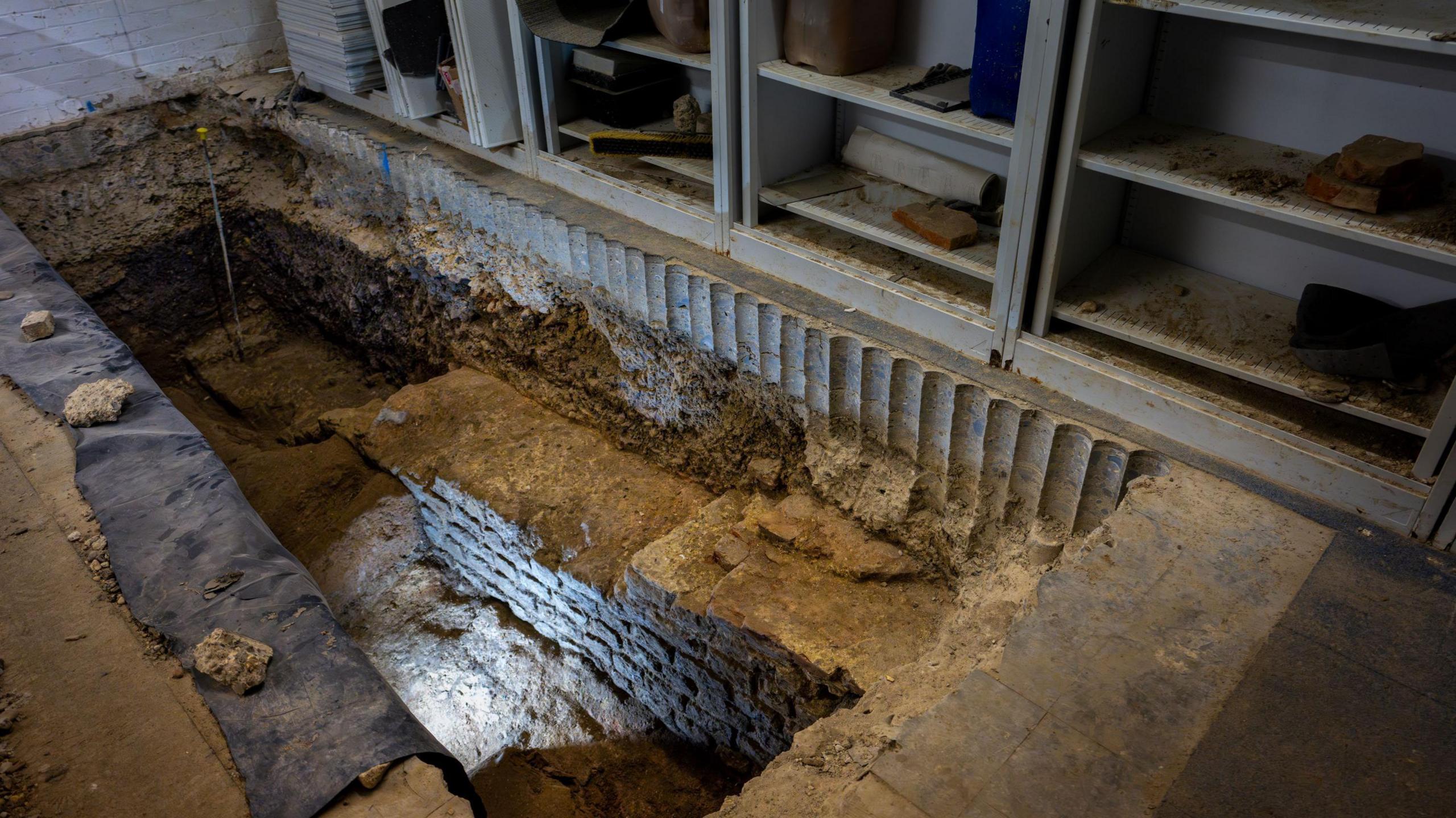 A large hole in the floor of a building, revealing a wall underneath
