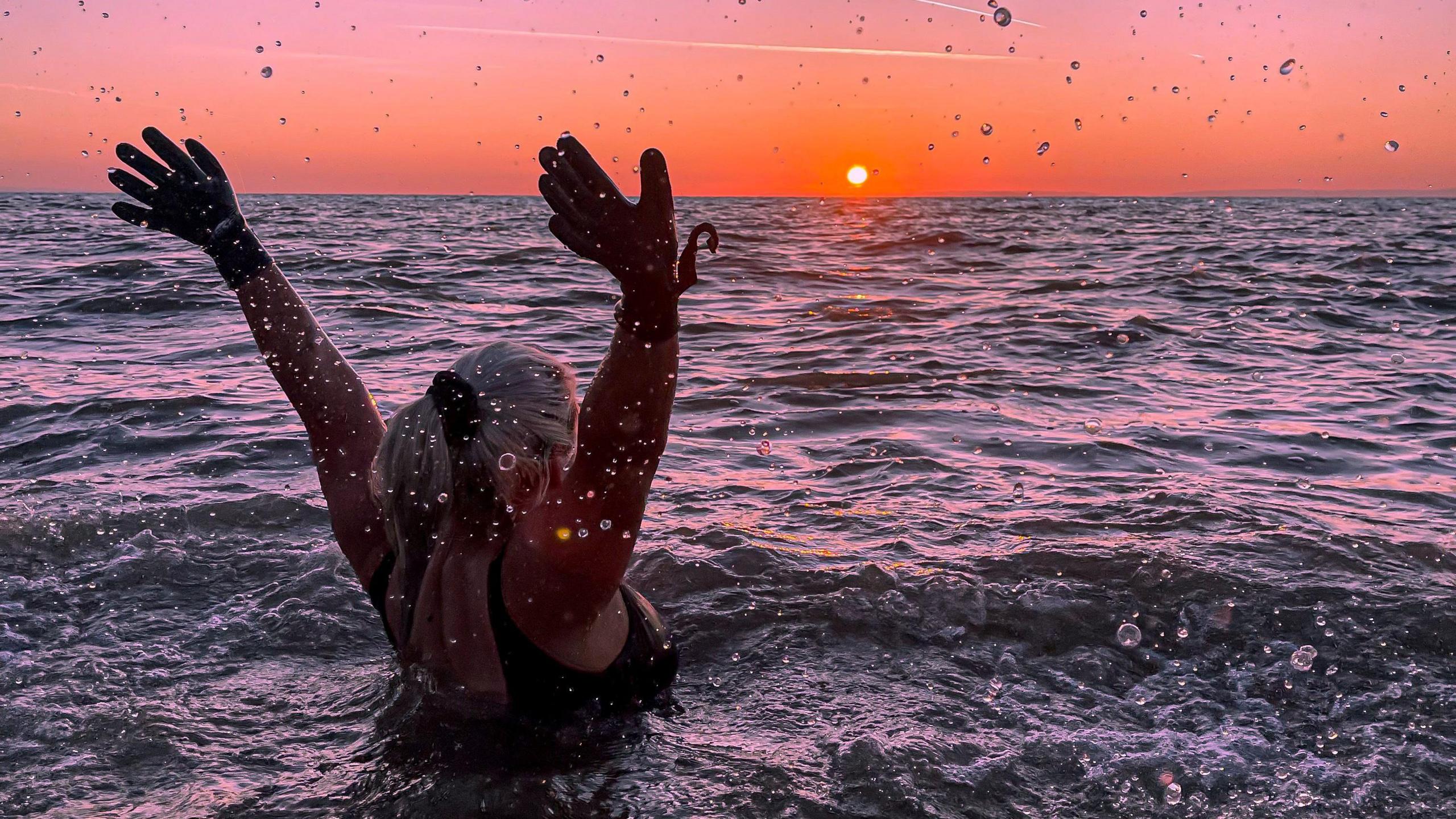 Jessie, a young woman, is seen in the sea as the sun sets over the horizon