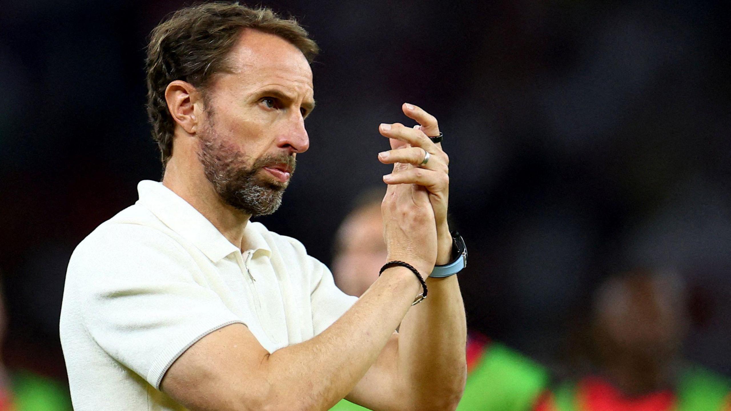 Gareth Southgate wearing a white polo shirt claps at an England game in July