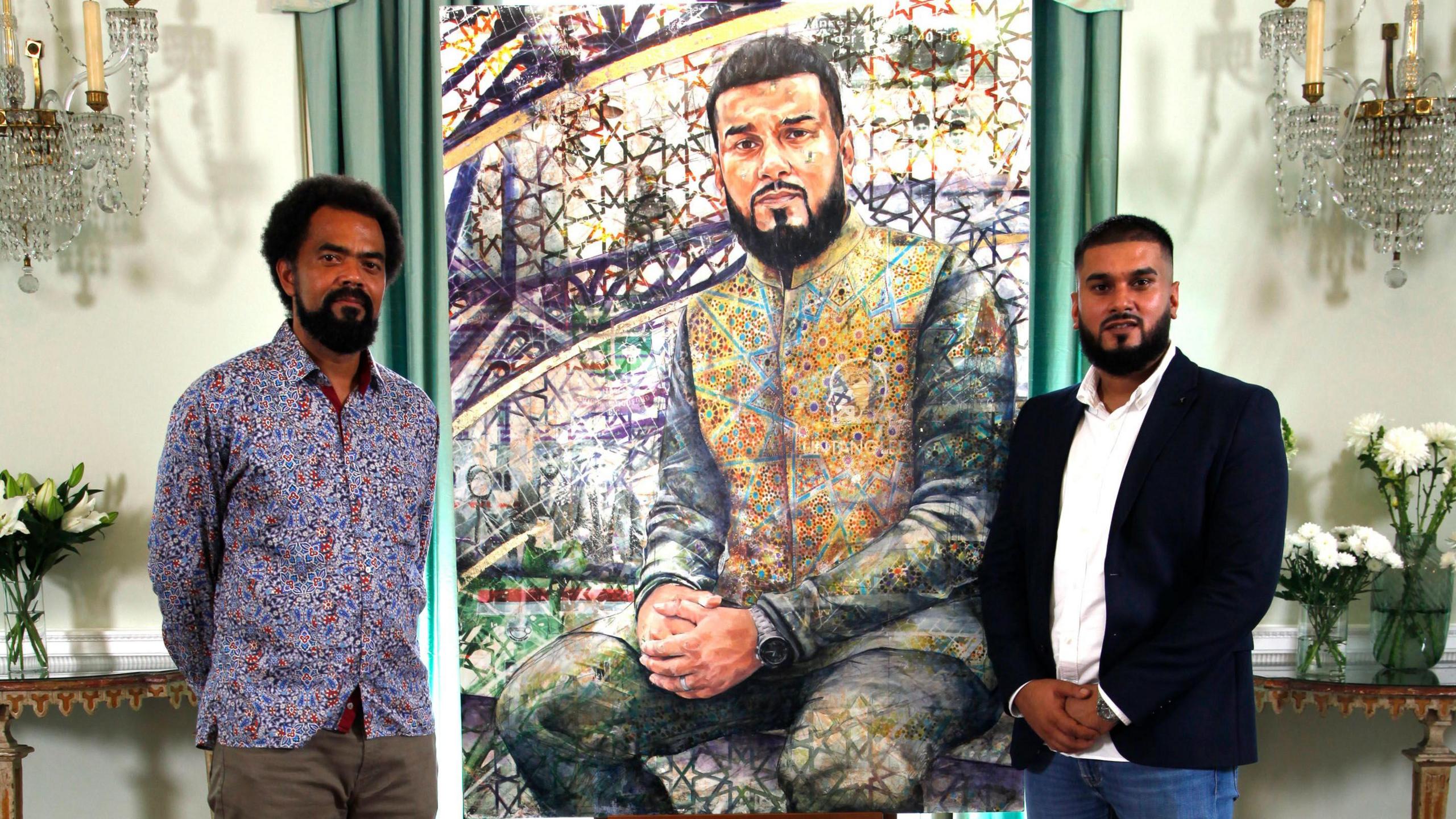 Jack, left, and Rizwan stand beside a vibrant, mosaic-inspired portrait of Rizwan in an elegant room with chandeliers and floral arrangements.