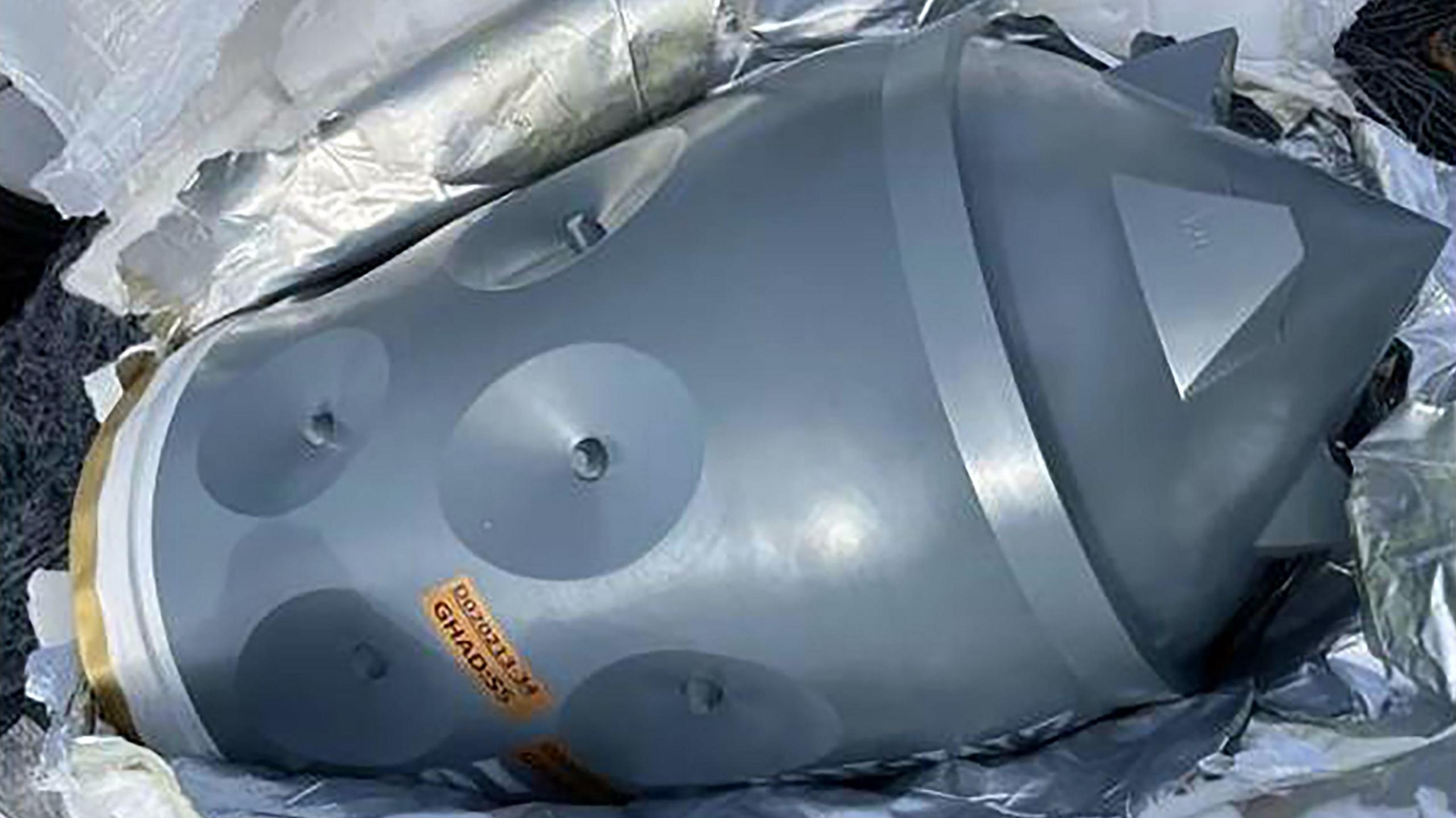 A close-up photo of a silver Iranian-made warhead. It appears to be lying on its side and surrounded by shiny silver packaging.