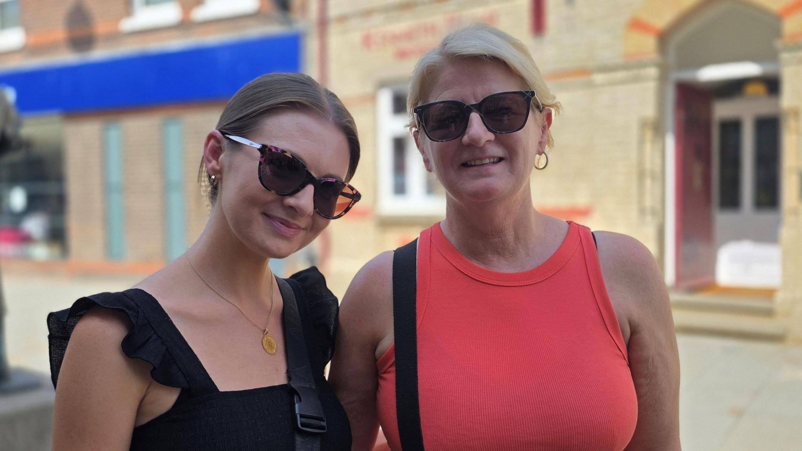 We can see two women standing in a street, both wearing sunglasses. Danielle is on the left, wearing a black sleeveless top. Her mum, Sharon, has a red sleeveless top on.