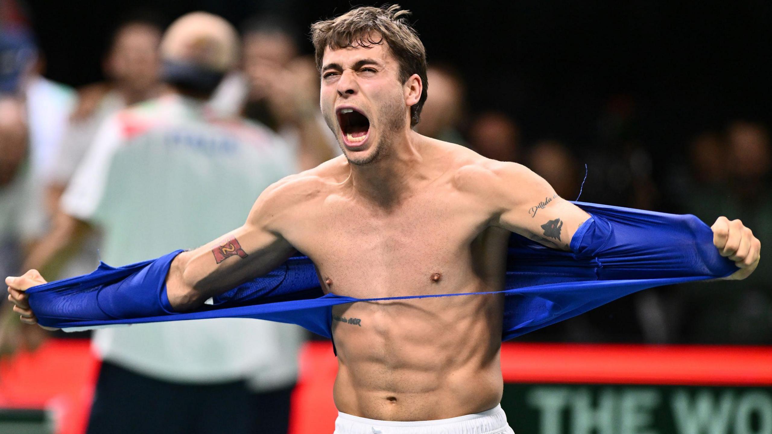 Flavio Cobolli tears off his T-shirt in celebration after sending Italy into the Davis Cup final