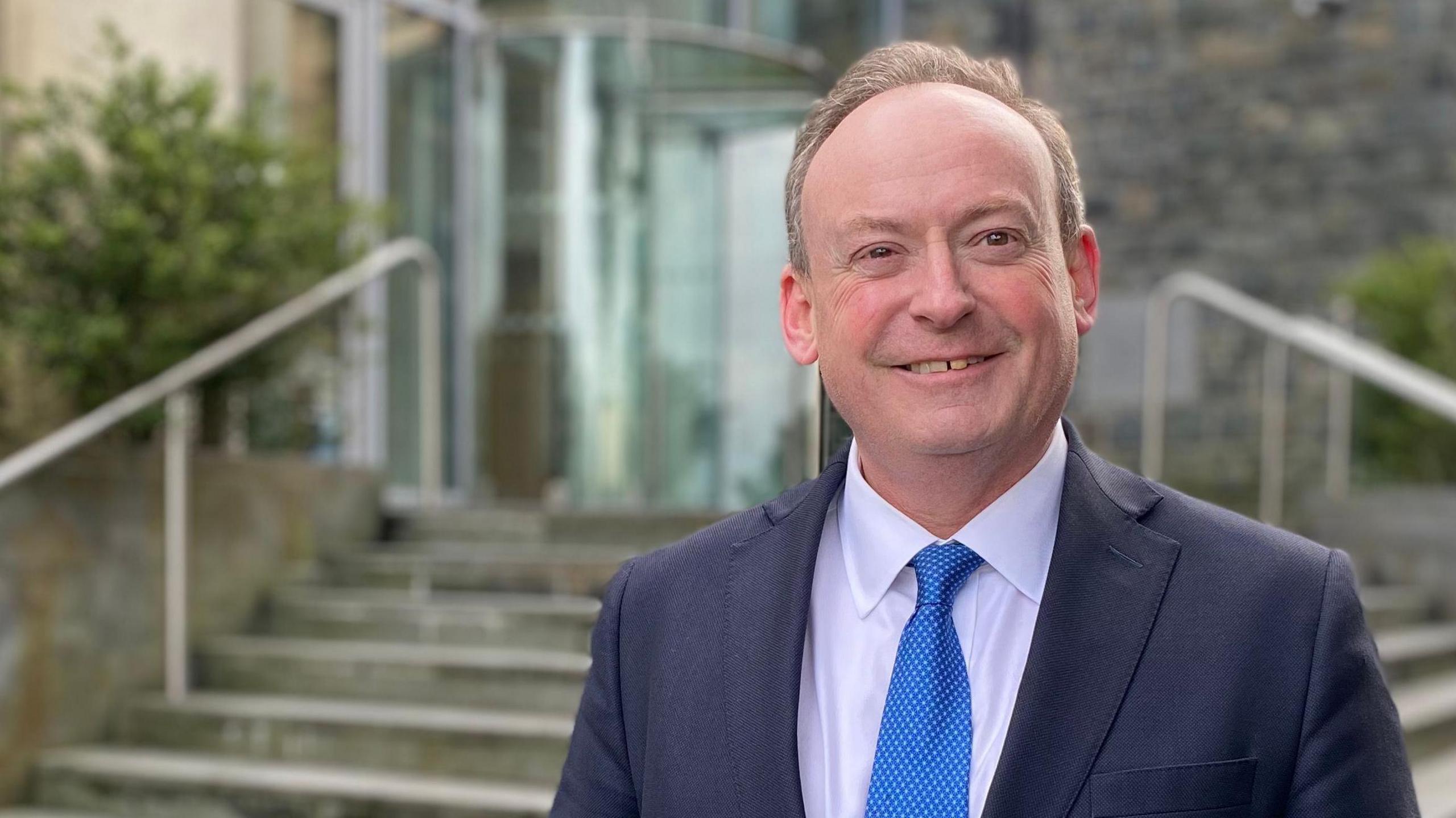 Man in a suit with a blue tie standing in front of the royal court