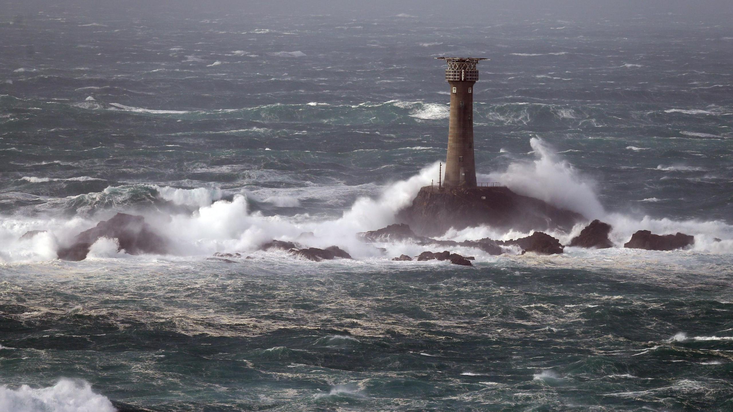 Longships Lighthouse is being blasted with waves whipped up by winds on a sunny day. 