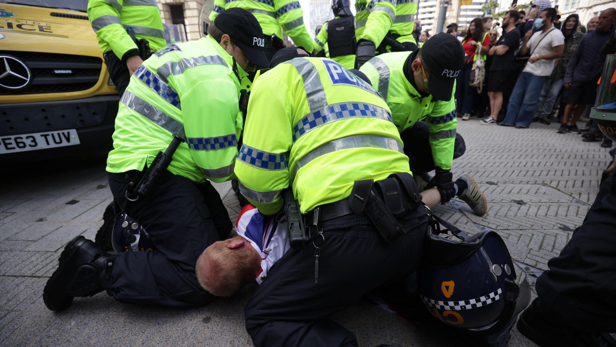 Three police in high viz vests hold a man down on the pavement