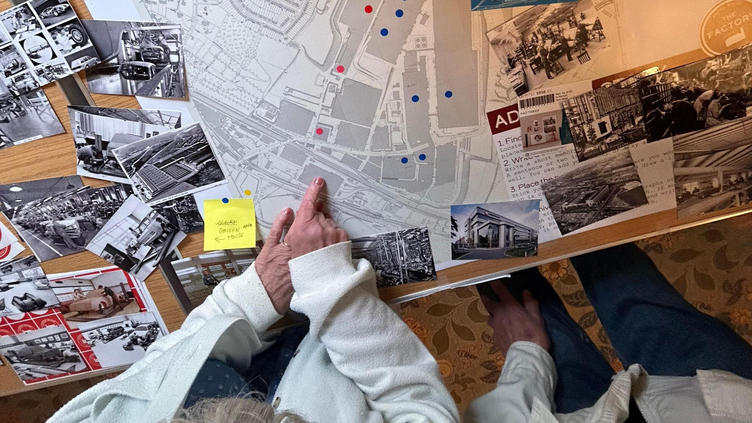 A view from above looking at a table with a large map indicating where Vauxhall's buildings used to be in Luton, with blue and red dot stickers on various buildings. There are also black and white photos dotted around. A woman's hands point to the map.
