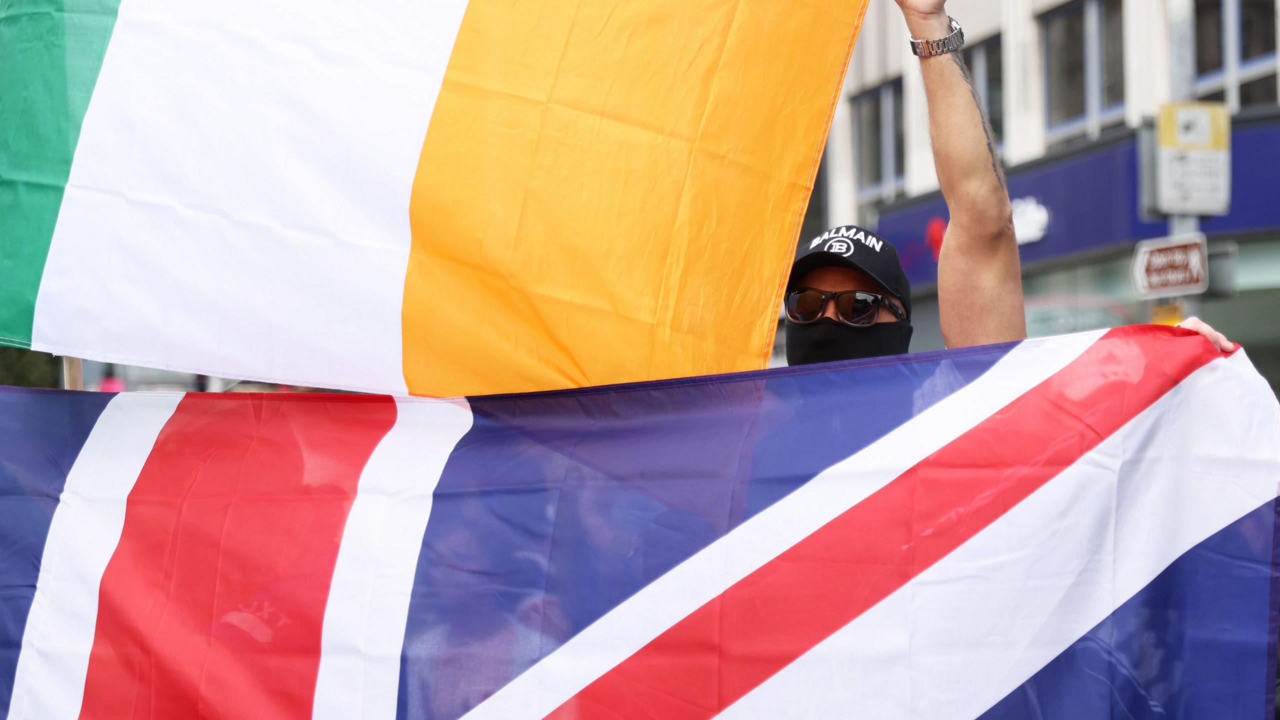 Masked man holding an Irish flag, with a large union flag also visible, during the Belfast protests