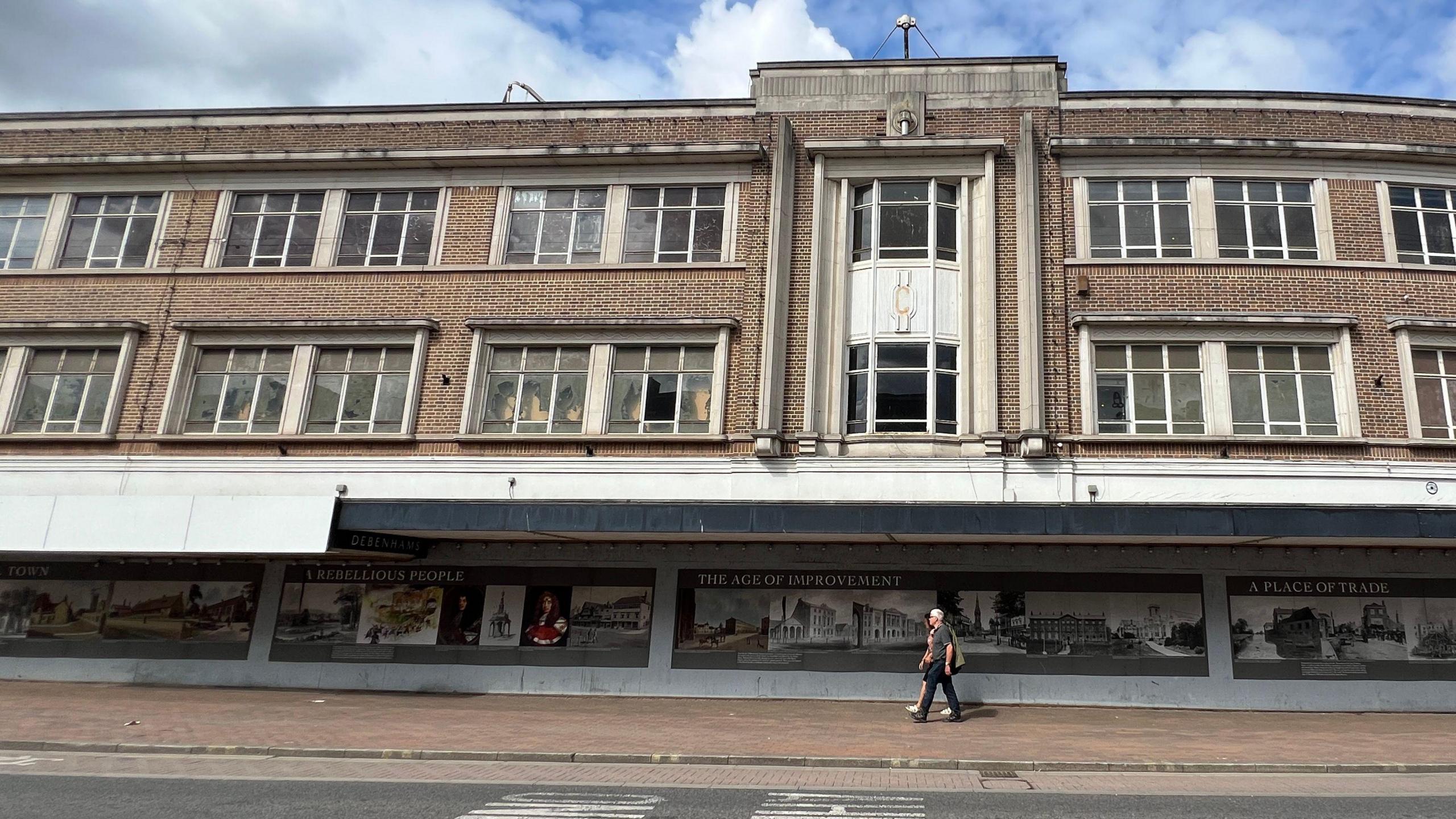 An exterior view of Taunton's former Debenham's shop. The building is closed, and a couple are walking in front of the building on the pavement
