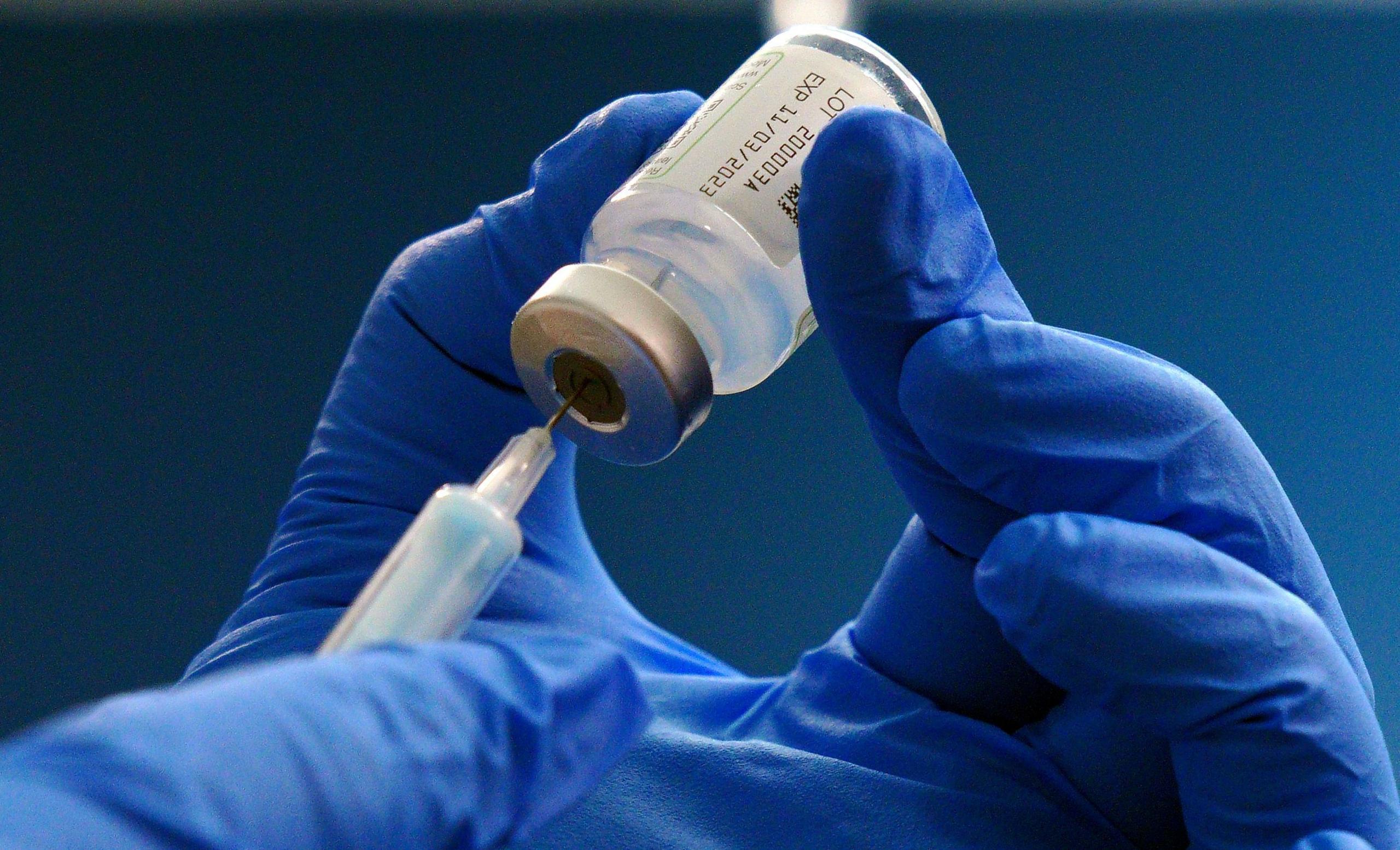 A gloved hand inserts a needle into a vaccination bottle. 