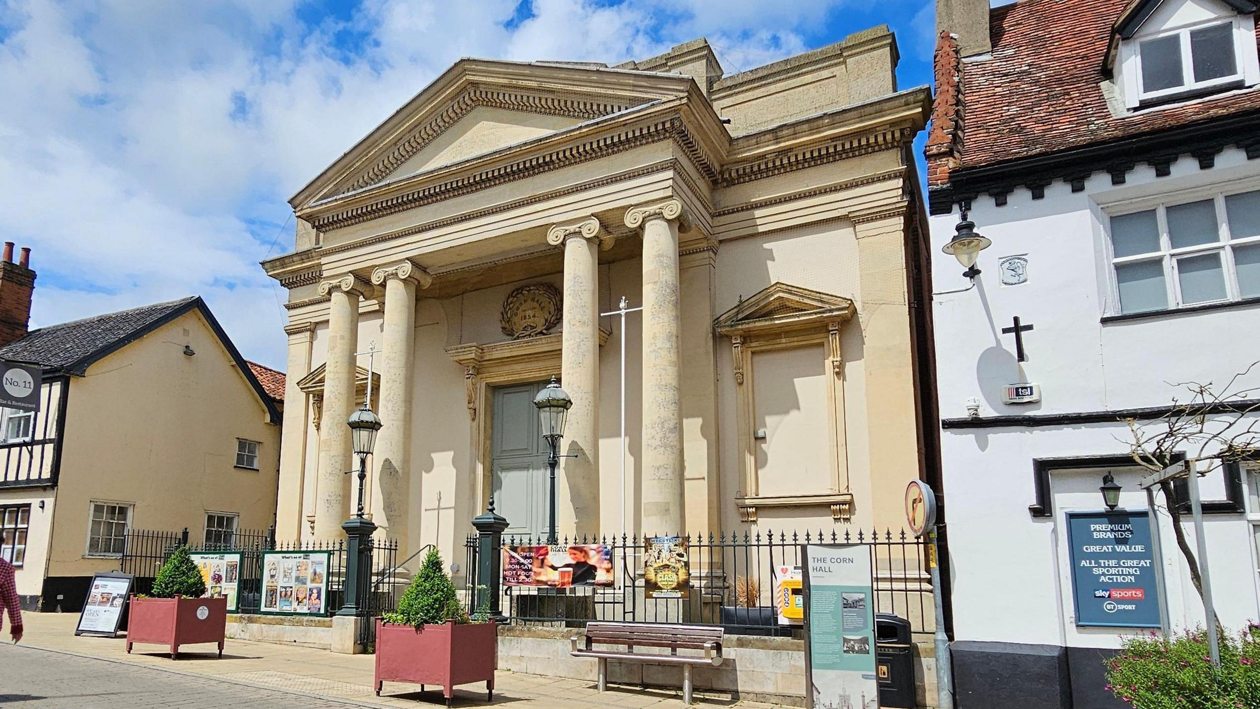 Diss Corn Hall, a large stone coloured building with a blue door, and pillars.