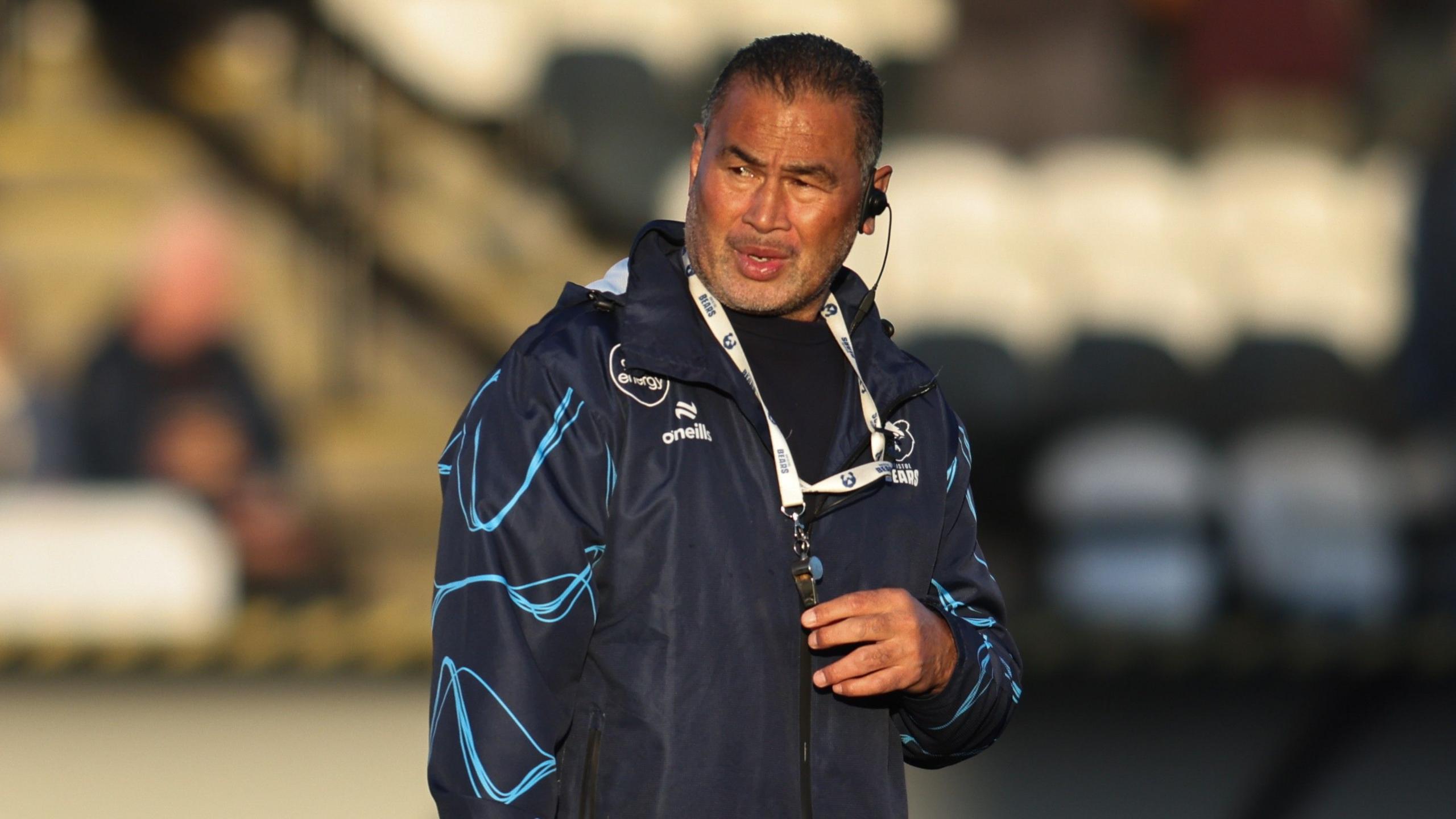 Bristol Bears director of rugby Pat Lam wearing a dark blue jacket and an ear piece, looking off into the distance after a Prem Rugby match.