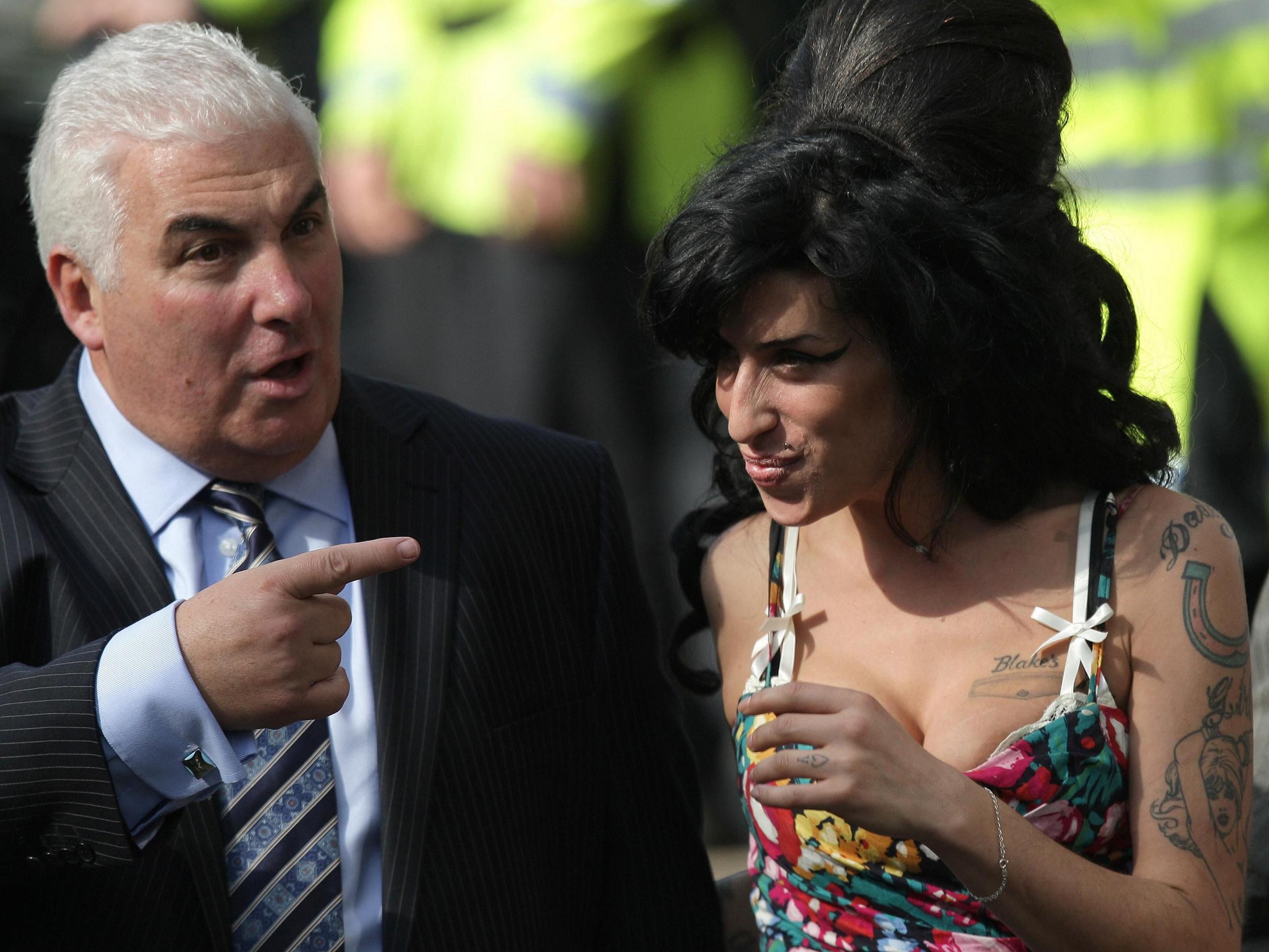 Man in suit and tie points at woman with big black hair in colourful top smiling