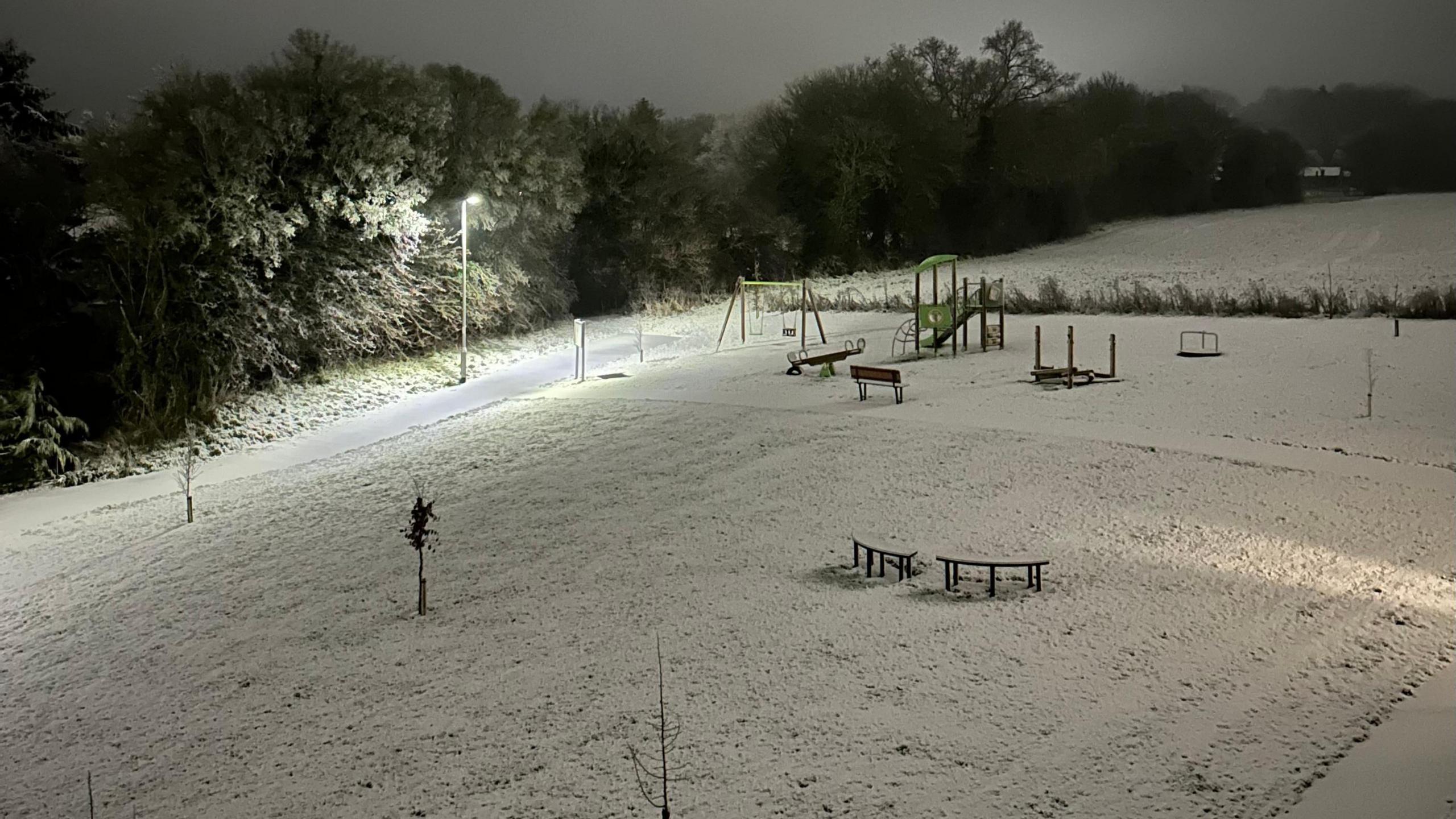 A snowy hill in Hadleigh, Suffolk, showing a snow covered playground and grass area. 