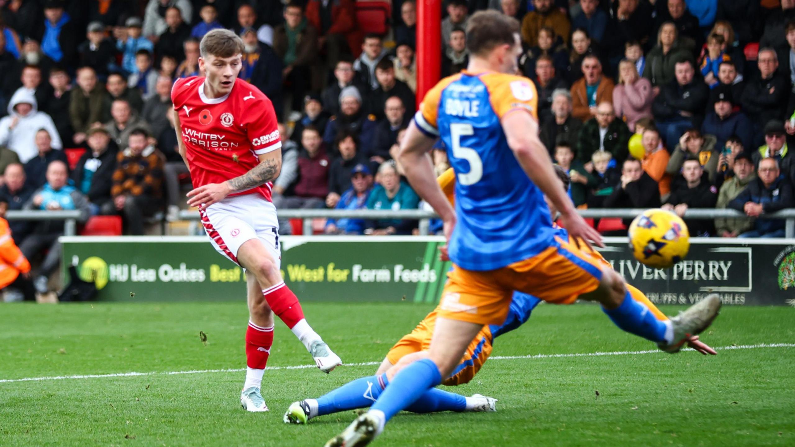 Owen Lunt shoots the ball through two Shrewsbury Town defenders' legs and into the net