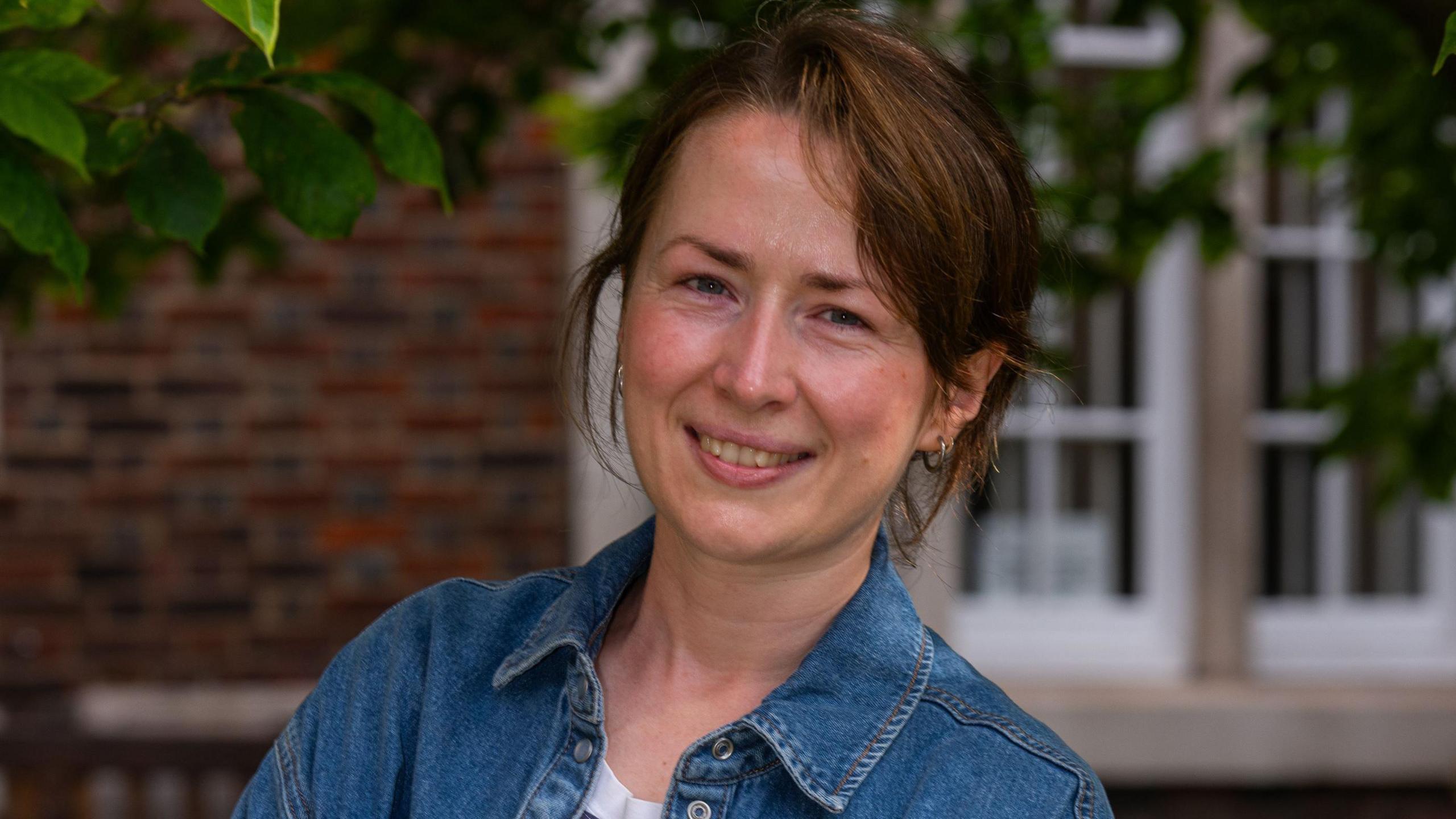 Fiona Packe wearing a blue denim jacket and small earrings, smiles at the camera