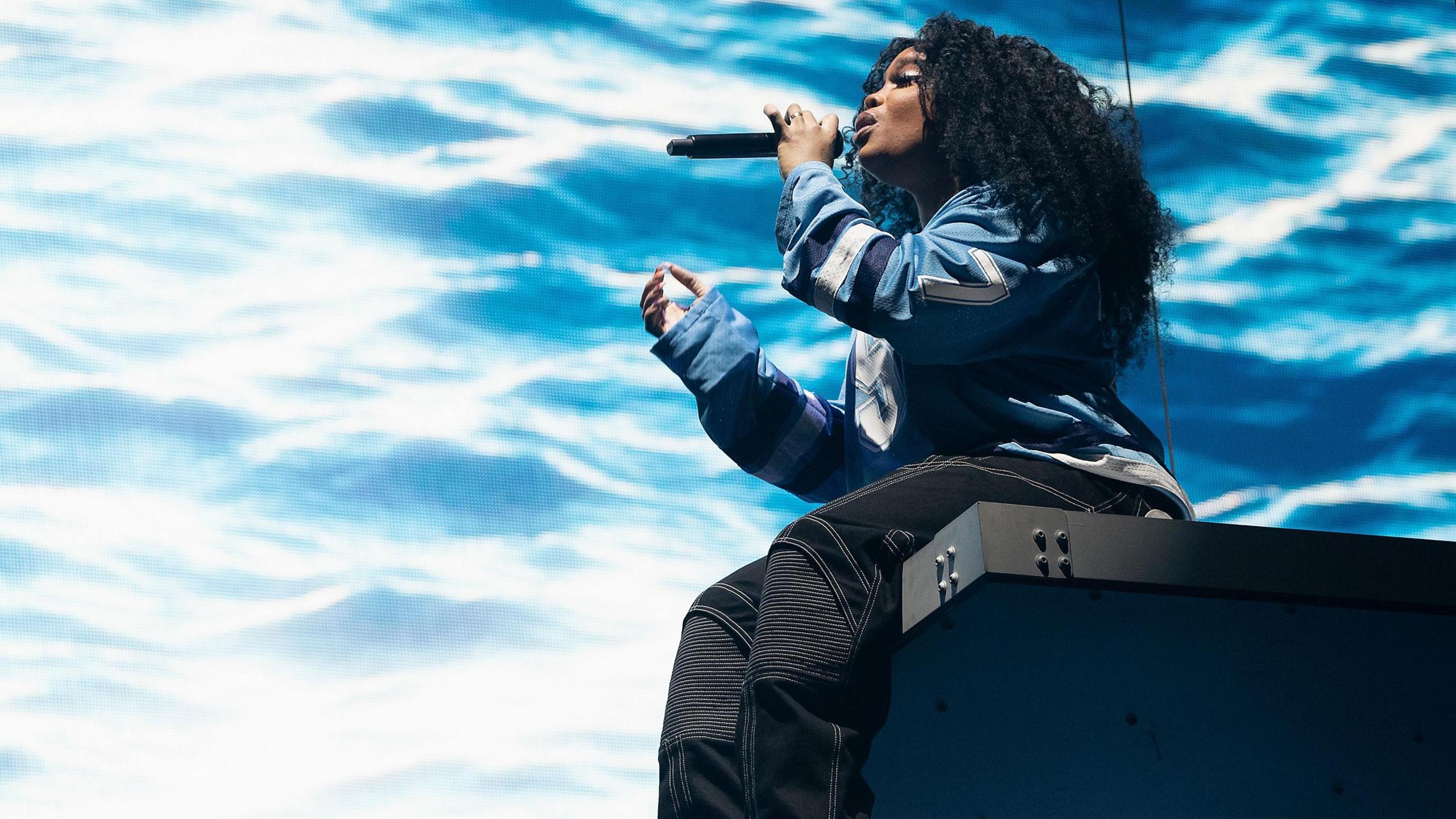 SZA sat on stage, in front of a stage backdrop which is meant to look like an ocean