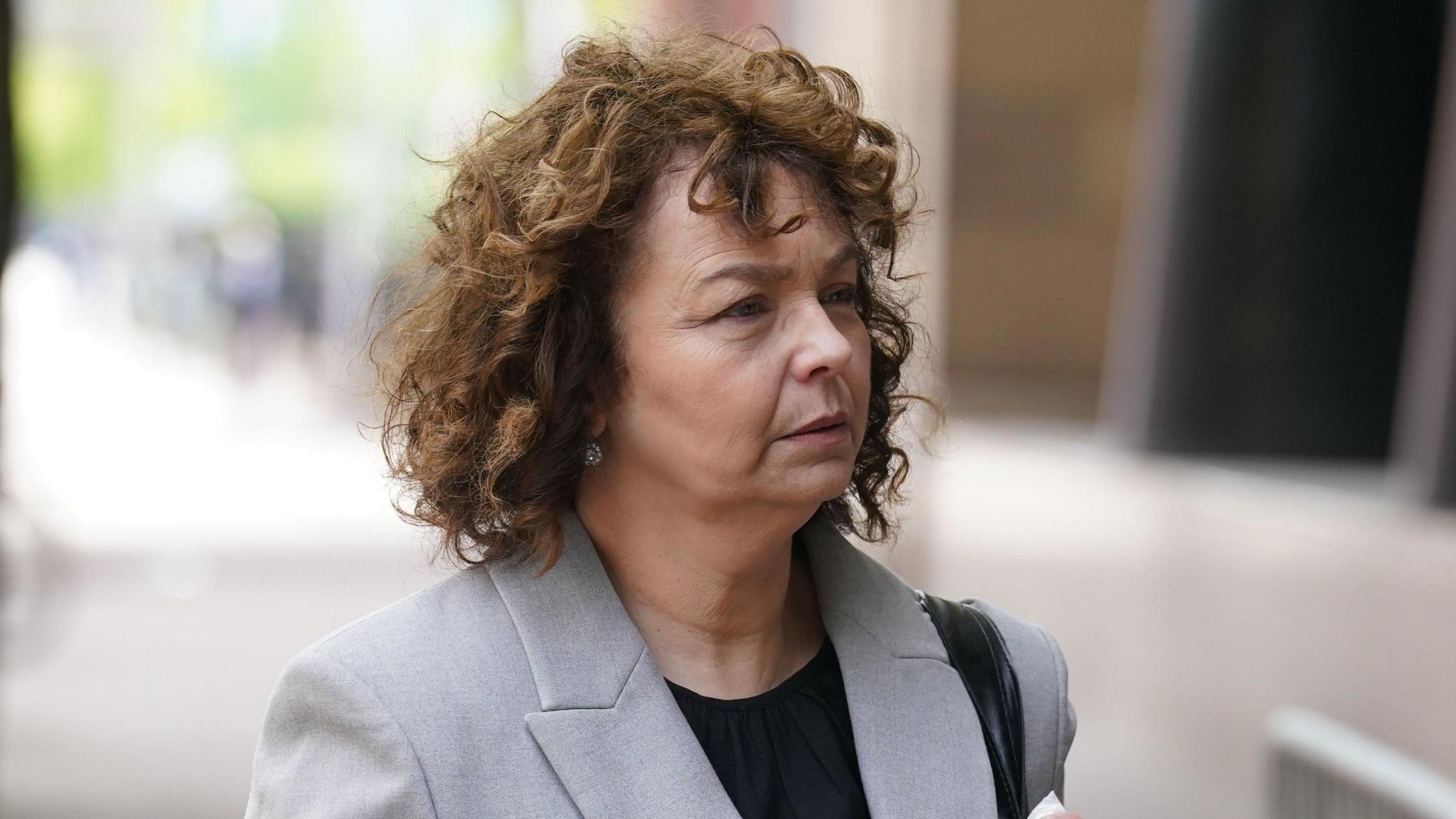 Carál Ní Chuilín is outside. She has curly brown hair. She's wearing a grey jacket with a black top. 