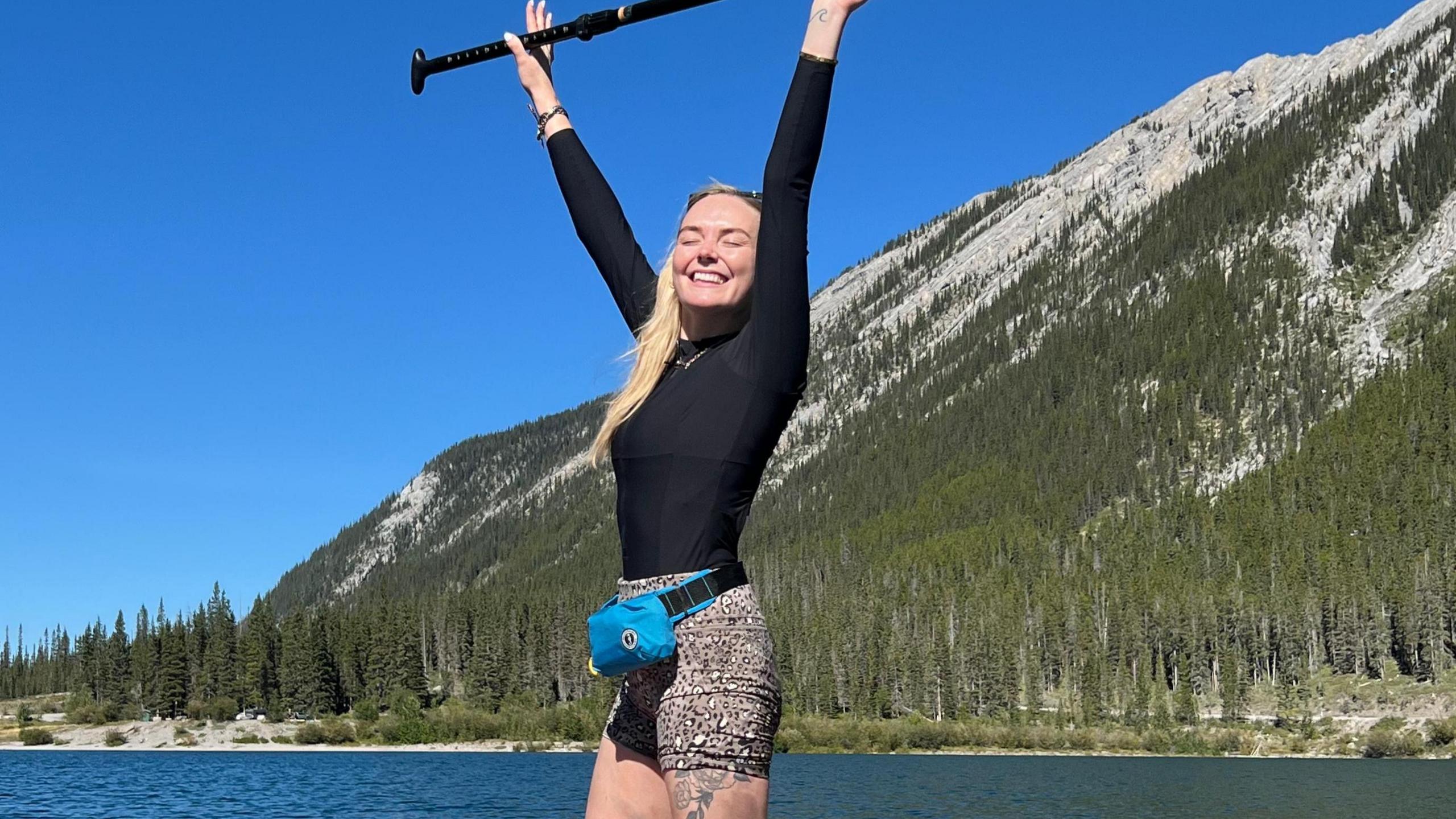 Georgie on a paddleboard on a lake, holding her paddleboard in the air