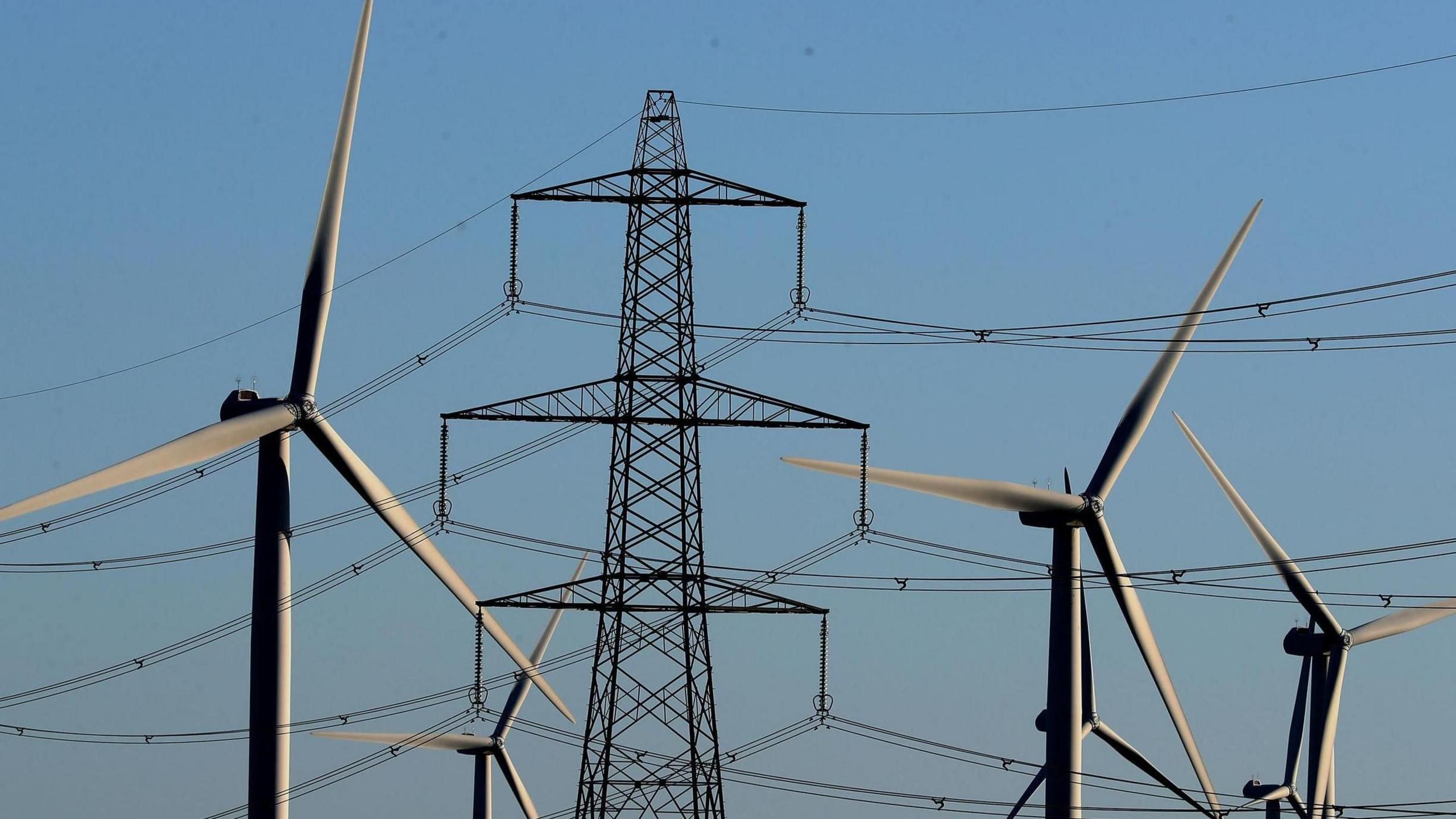 Wind turbines with an electricity pylon against a clear blue sky