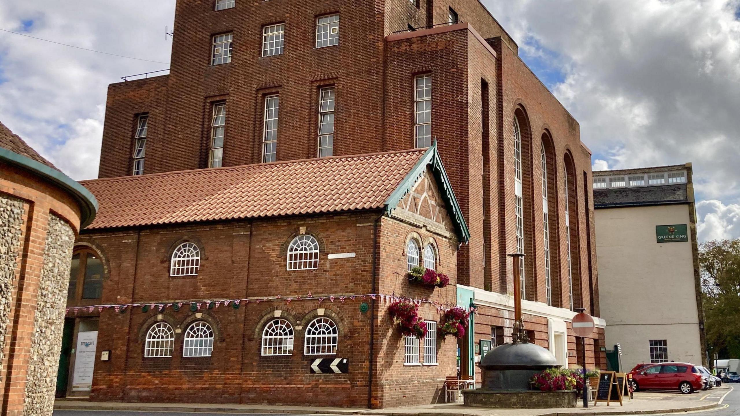 Greene King's Watergate Brewery, in Bury St Edmunds. It is predominantly an orange-coloured brick building in front or a cream-coloured building, which is displaying the Greene King logo.